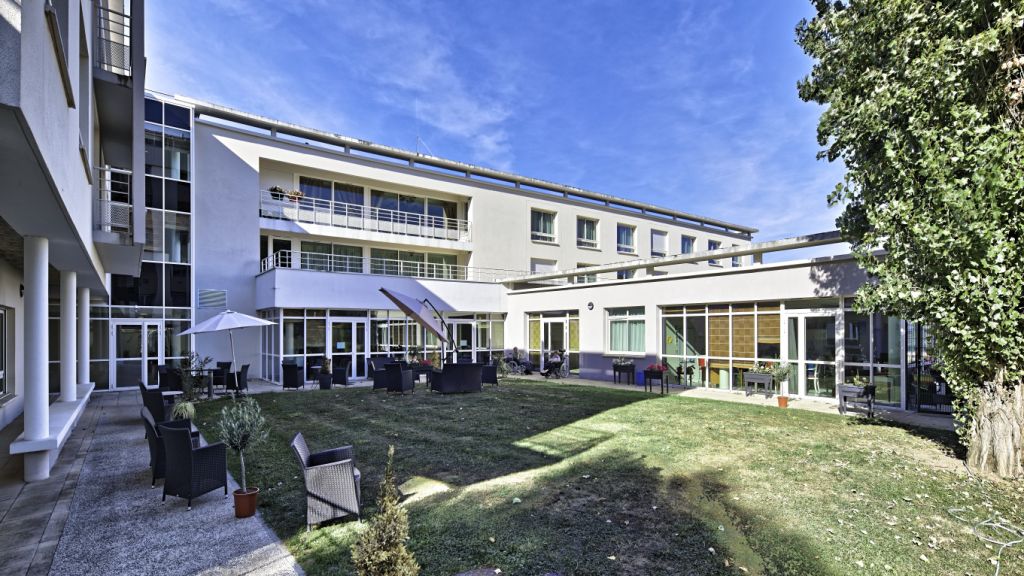 Residential building with yellow and white facade, outdoor garden landscaping, green lawns, and blue sky