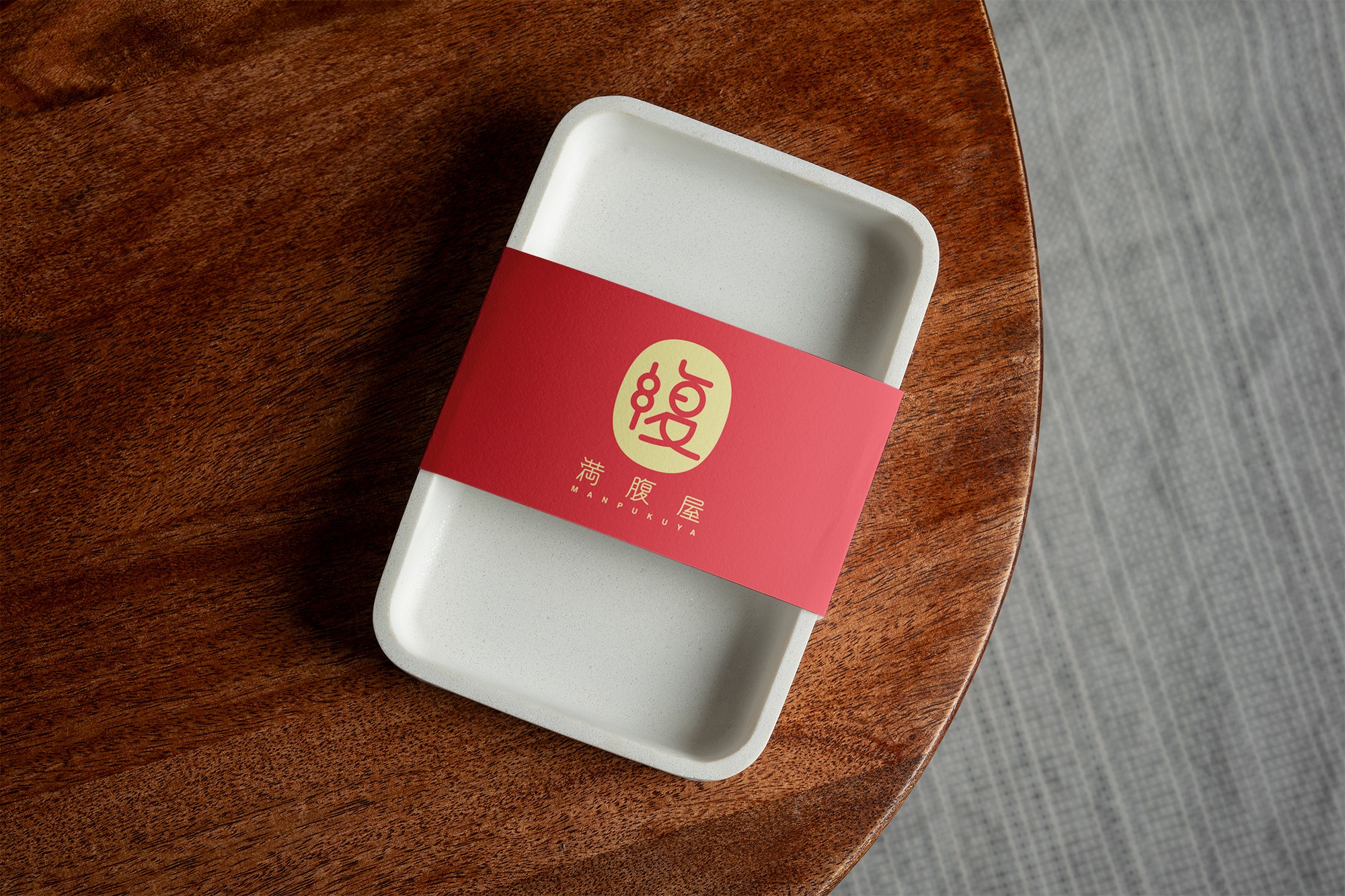 這張圖片展示了滿腹屋的外帶盒設計模擬，餐盤上綁有一條紅色的紙卡腰封，上面印有滿腹屋的品牌識別。