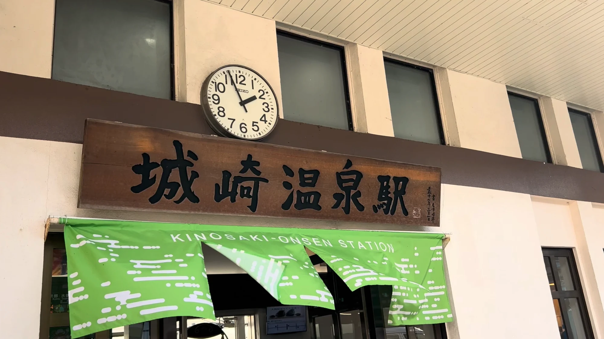 The Kinosaki Onsen station name board beside a green banner at the platform edge.