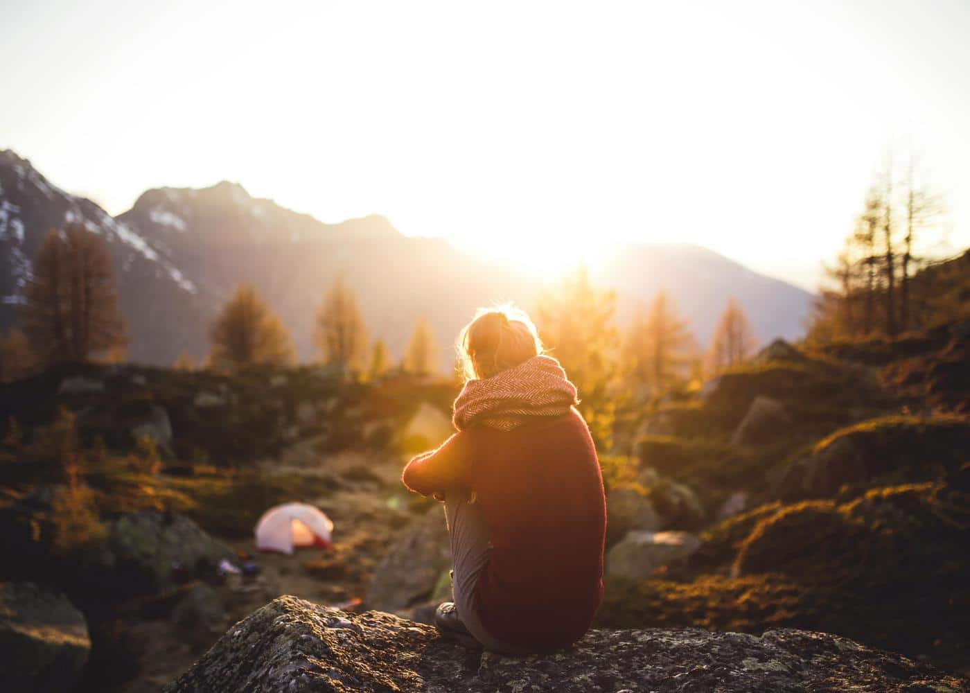Woman sitting on a rock and watching the sunrise over the mountain