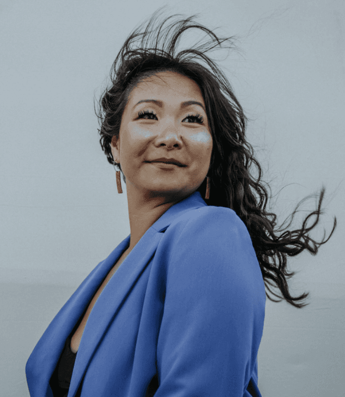 Young man in a black turtleneck and blazer stands outdoors, smiling softly. The background is blurred, conveying a warm, professional tone.