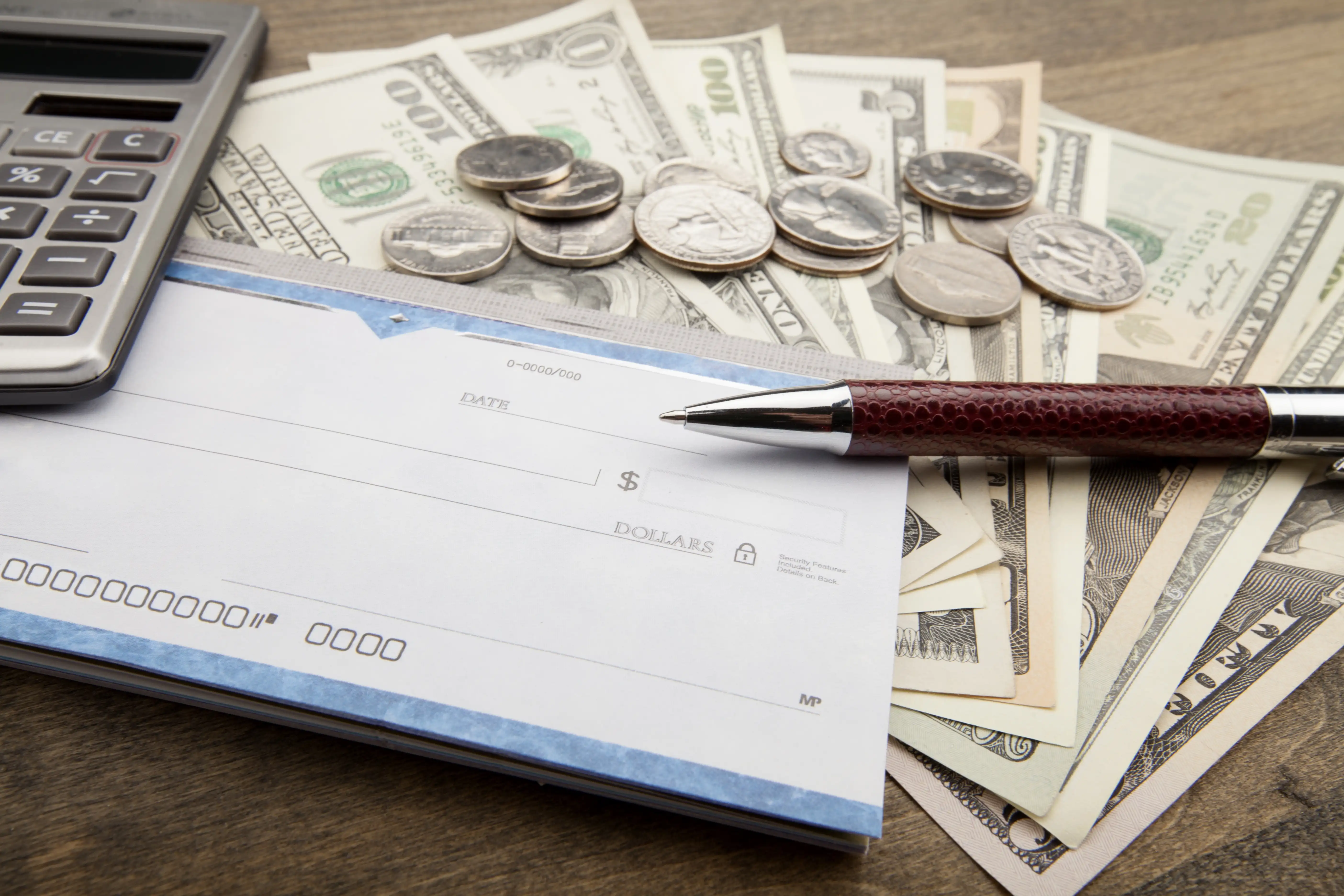 Desk setup with a checkbook, pen, calculator, US currency, and coins illustrating wage and hour damage calculations for Central Valley workers