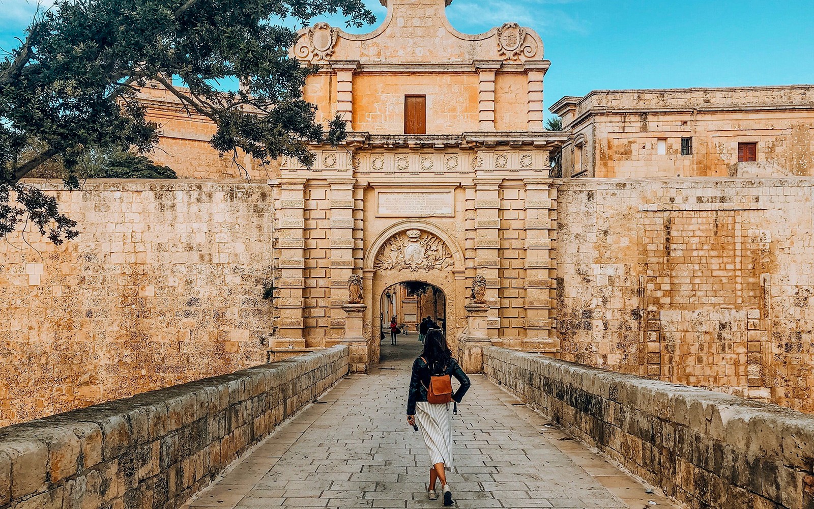 Person walking towards Mdina Gate, Malta, on a half-day tour including Dingli Cliffs and San Anton Gardens.