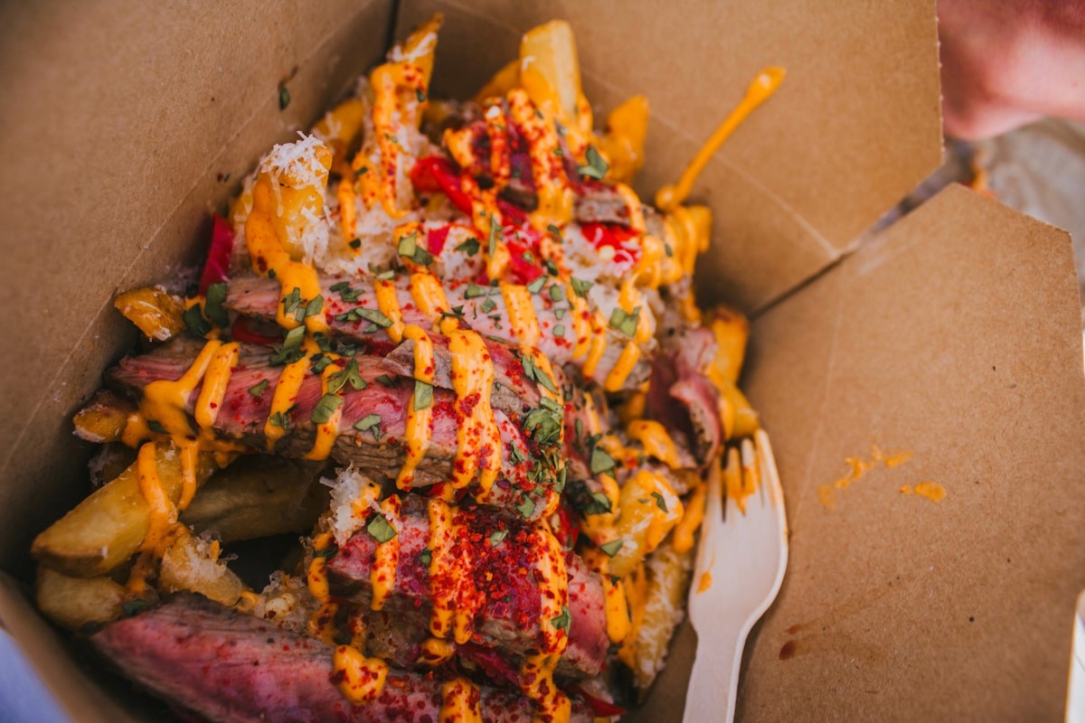 Loaded fries with melted cheese and sauce in a paper tray