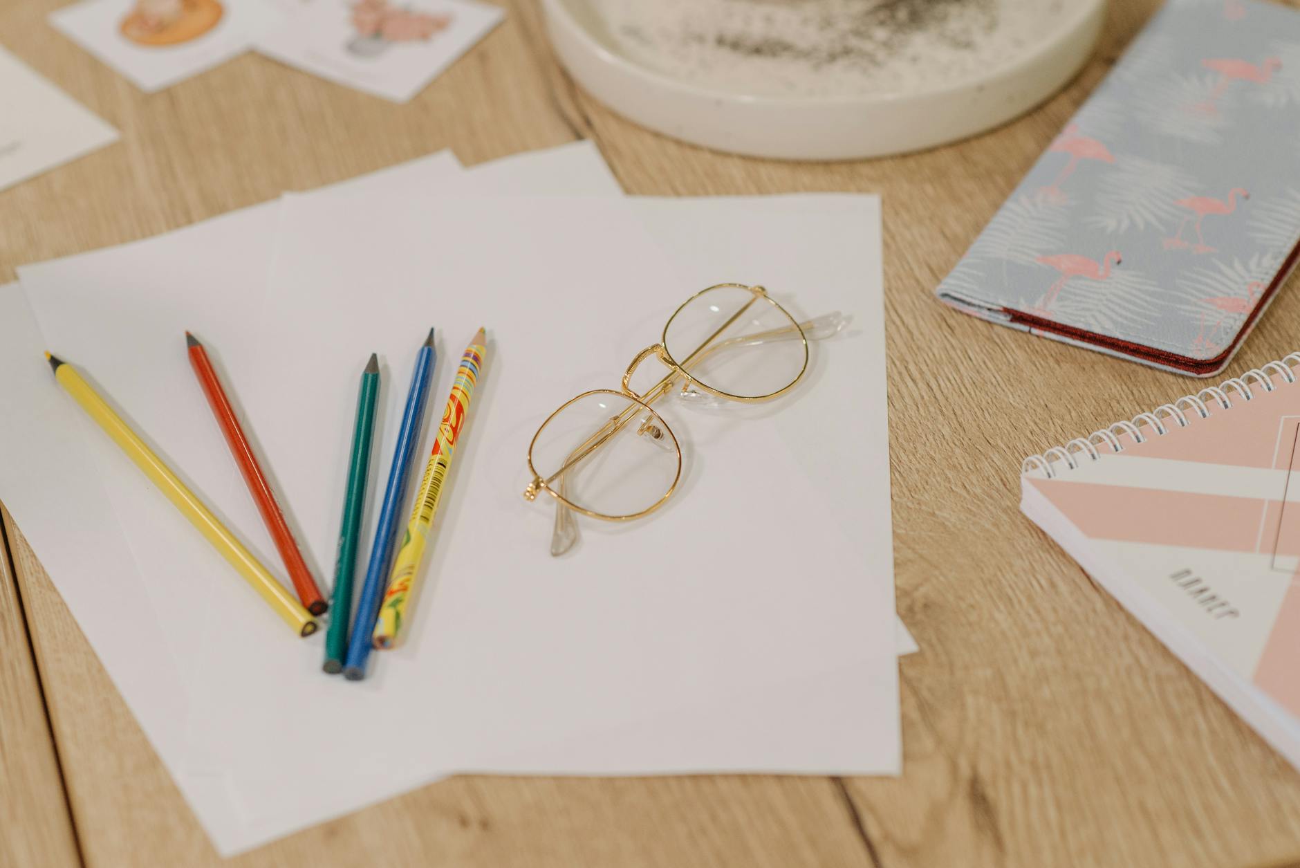 A tidy wooden desk featuring a stack of graded notebooks, a pair of glasses, and a sharpened pencil.