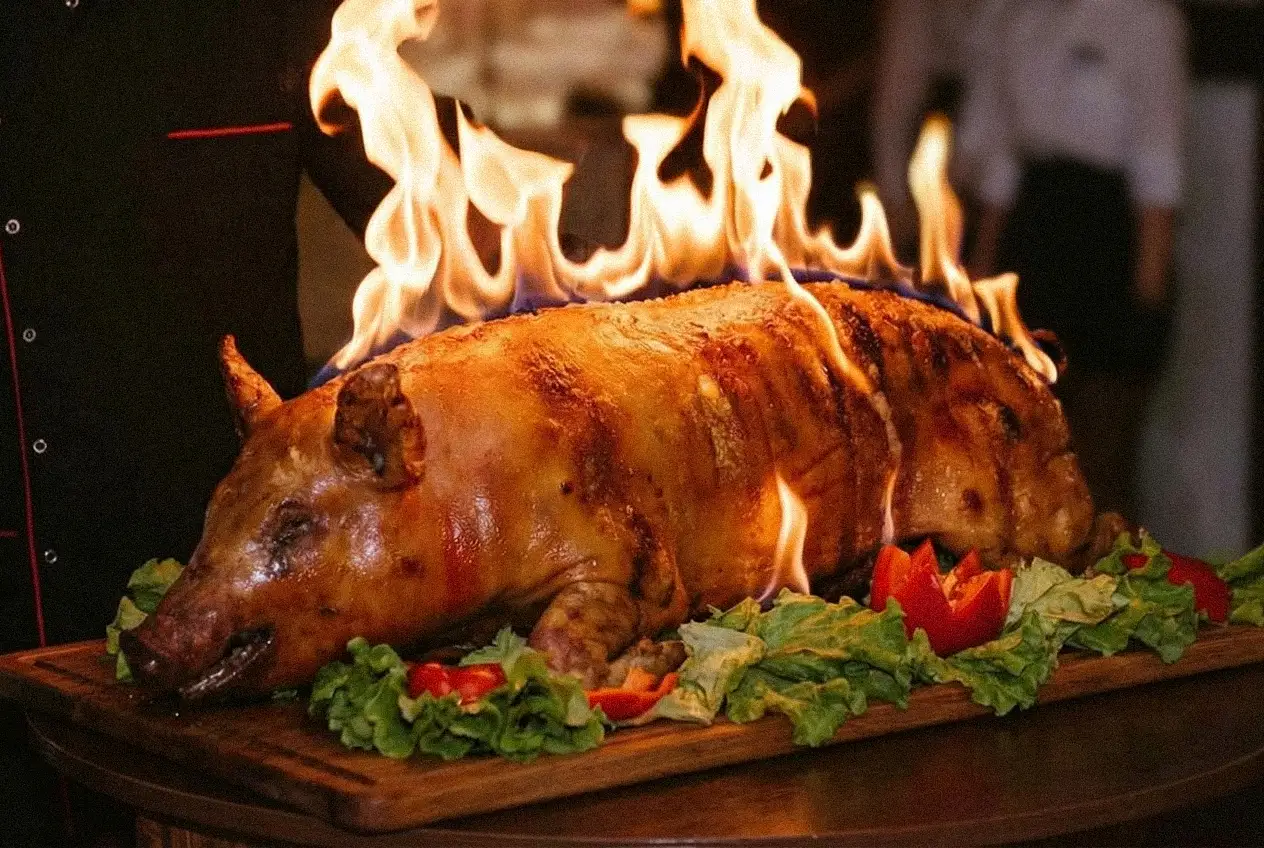 Pieczony prosiak podawany w efektownym płomieniu, ułożony na półmisku z warzywami, we Wrzosowym Tartaku
