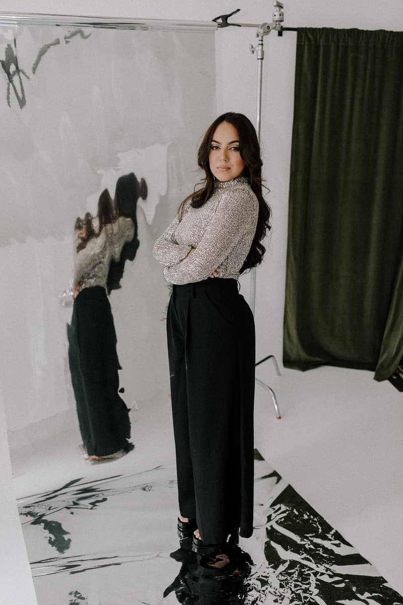 A full-body shot of a model crossing her arms in a silver top and black trousers, standing against a reflective surface during a creative Mylar shoot at Revelator Studio in Shreveport.