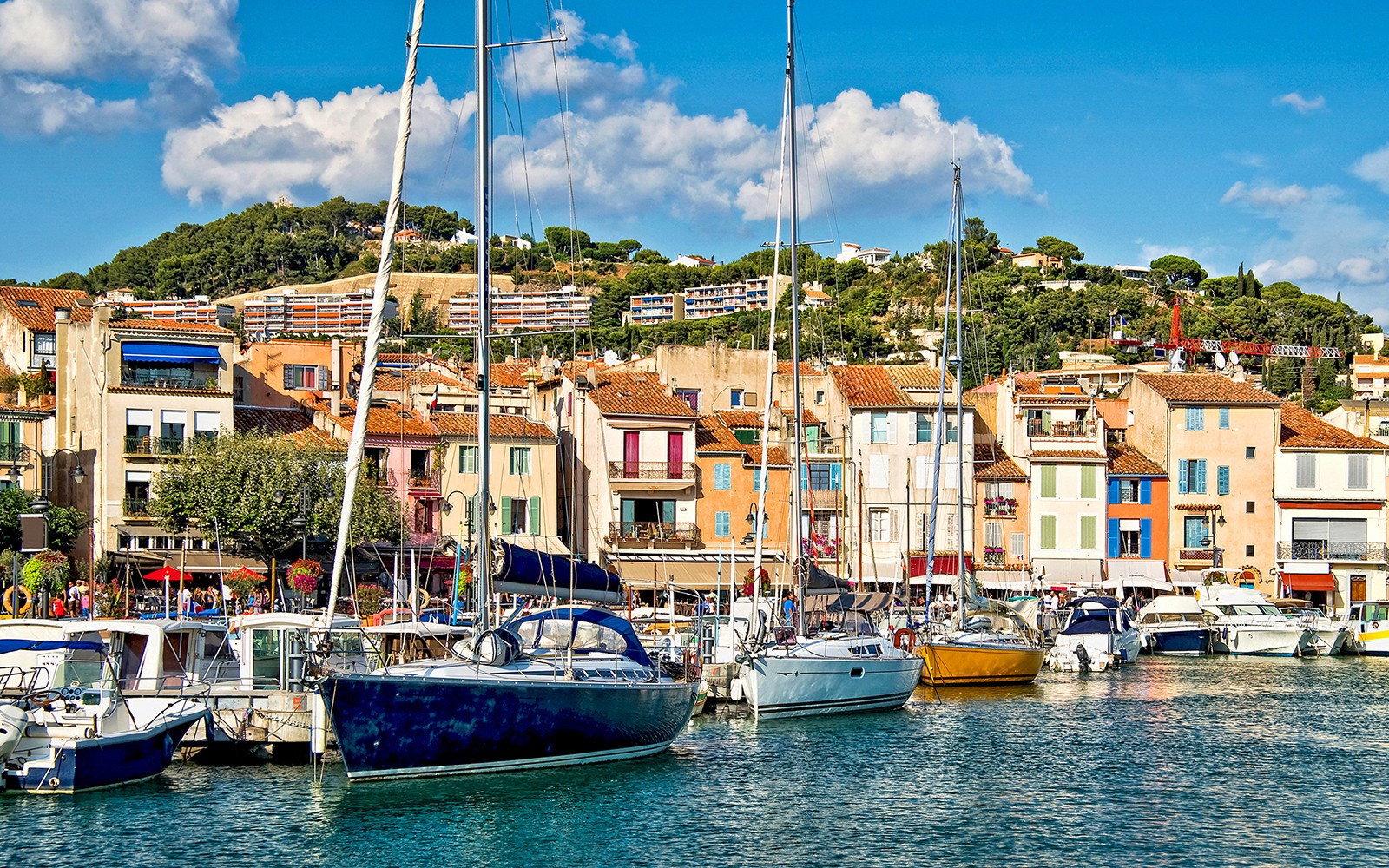 Boats docked at the colorful harbor of Cassis, France, with hillside buildings in the background.