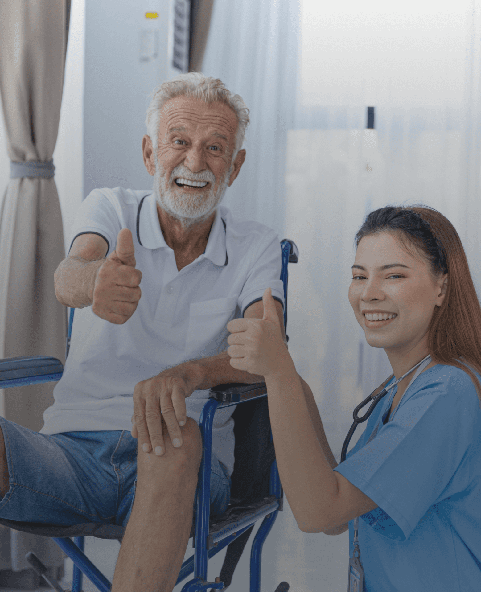 Older man in a wheelchair giving a thumbs-up beside a smiling caregiver.