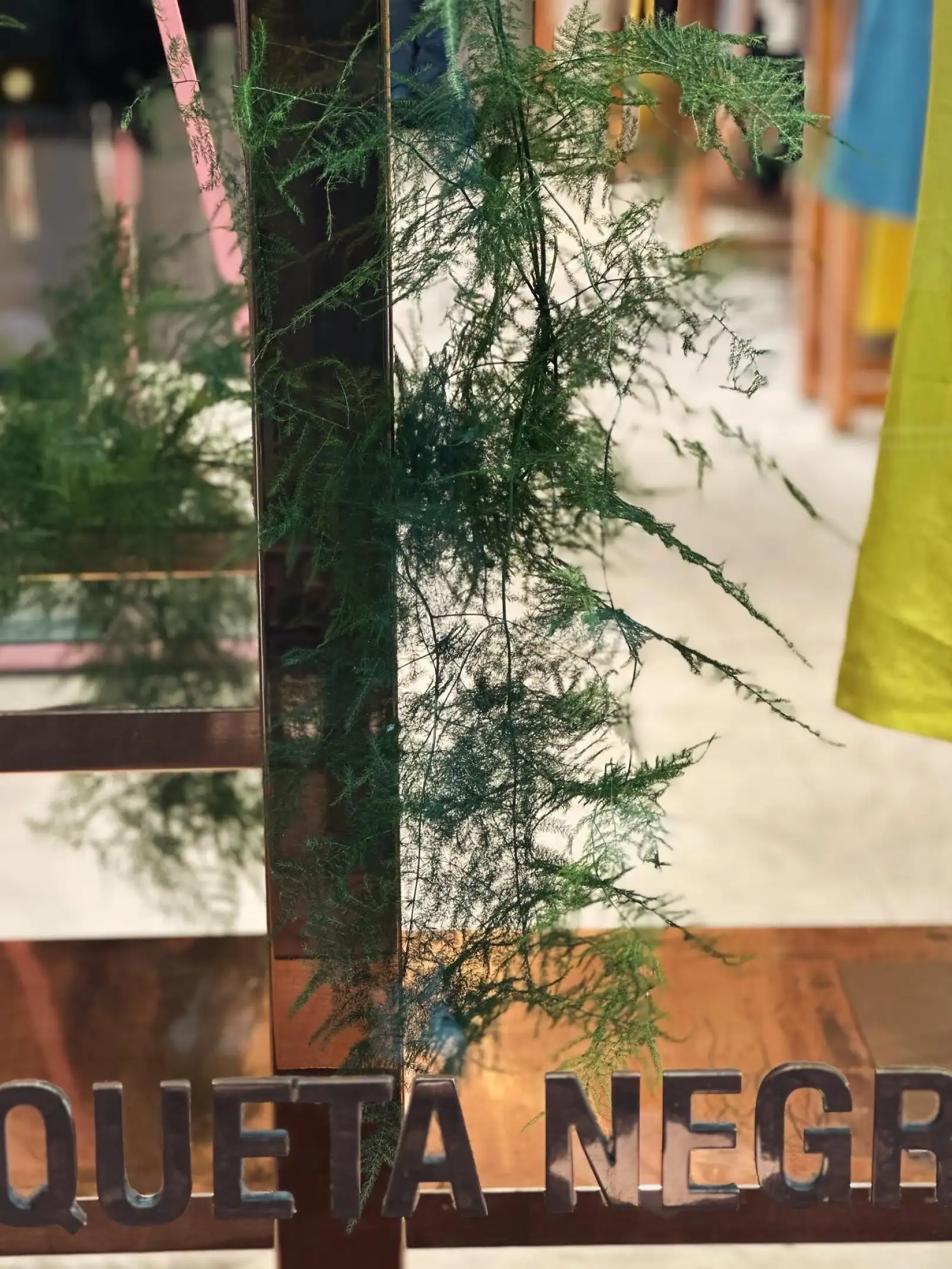 Detalle de follaje verde suspendido sobre estructura metálica para escaparate con estética natural y ligera.