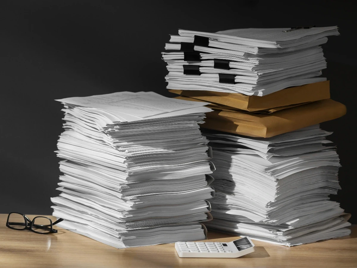 Mehrere hohe Stapel von Papierdokumenten liegen auf einem Holztisch