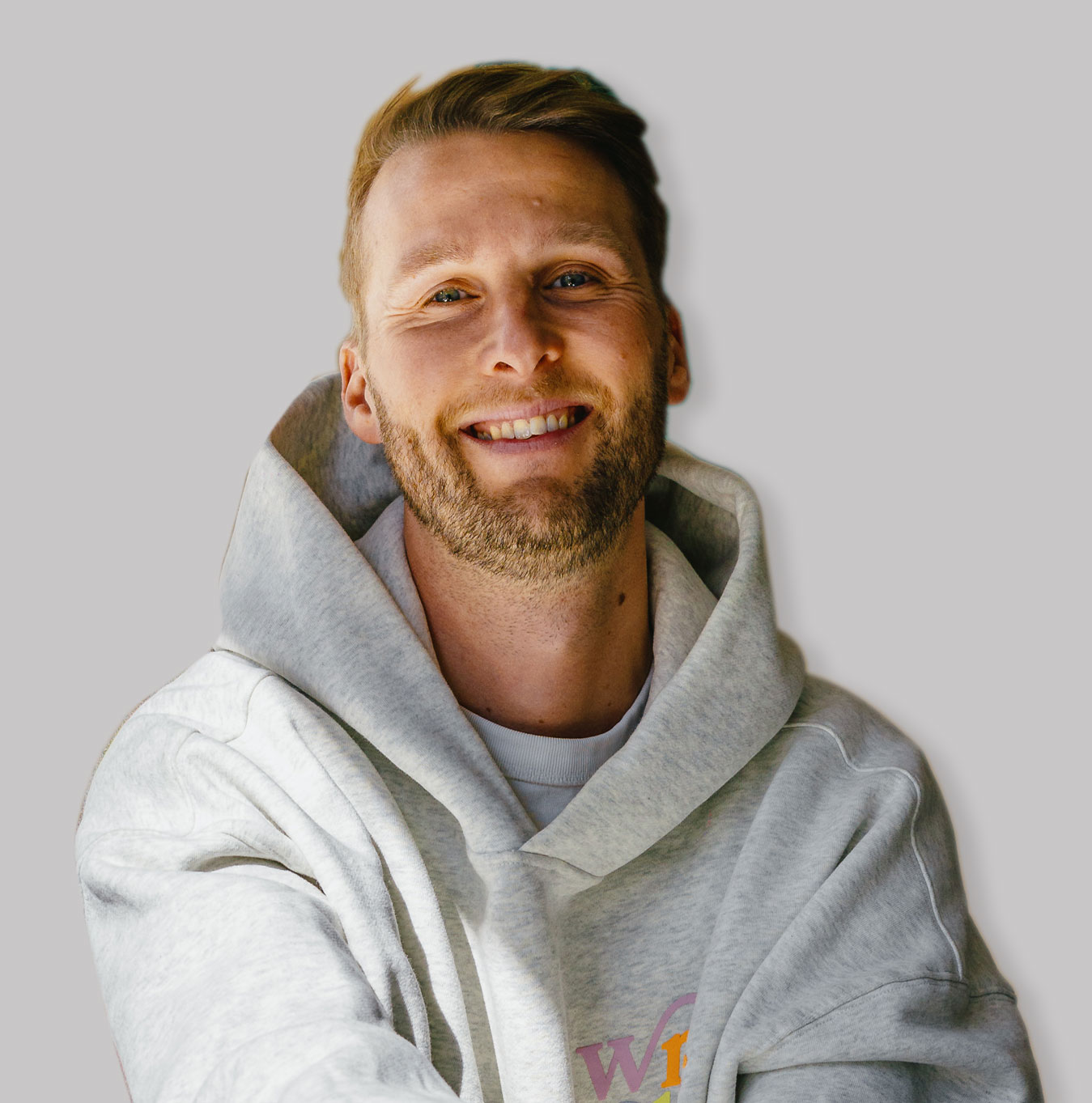 Casual studio portrait of a bearded man with curly hair in a white shirt, arms crossed, on a light gray background.