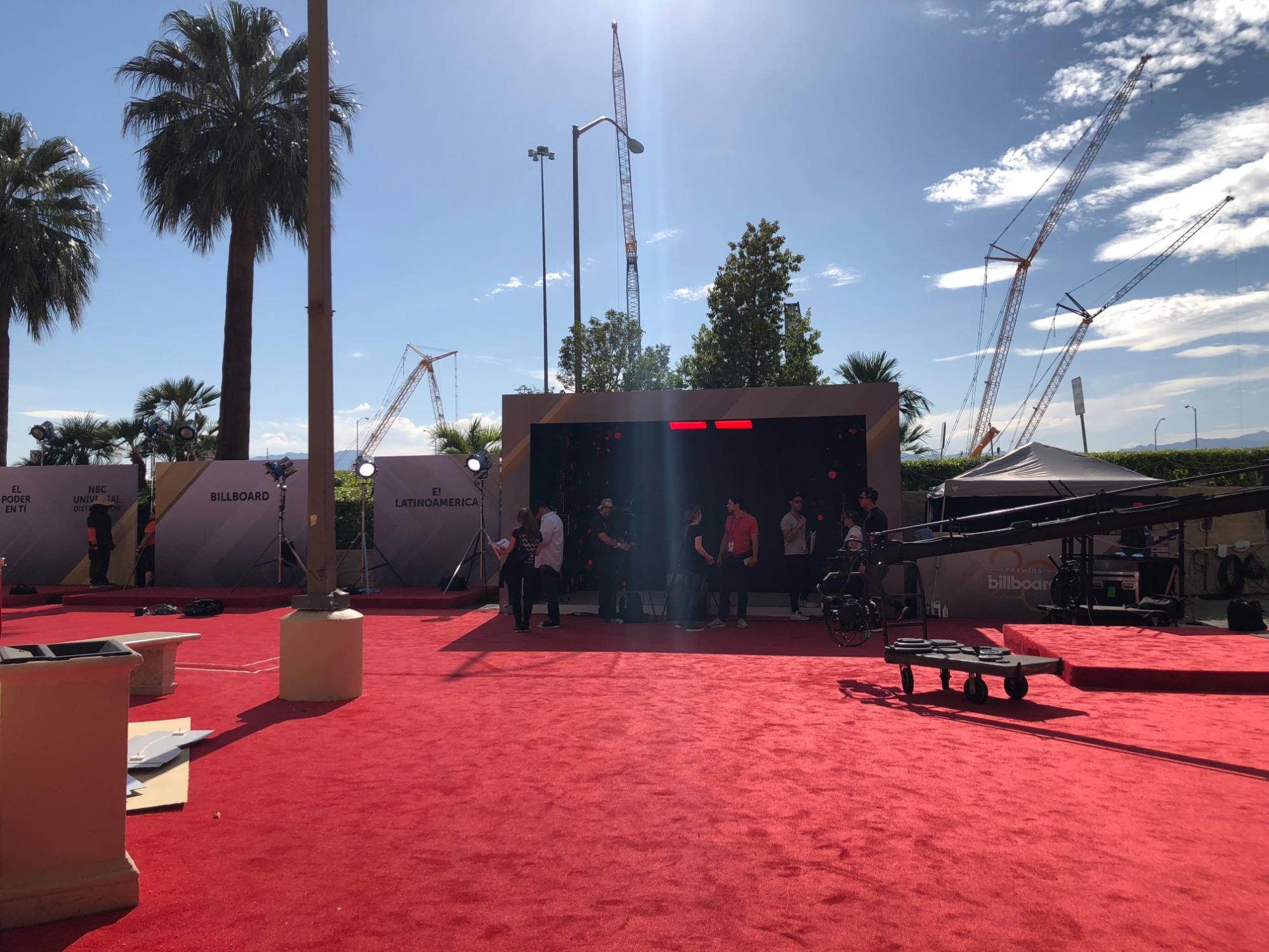 Wide view of an outdoor red carpet production setup with branded walls, lighting, camera equipment, and experiential activation area.