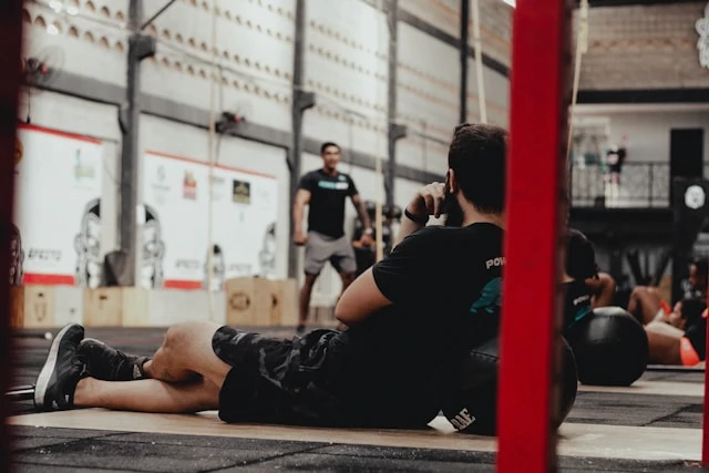 Man training in a gym while another person stands in the background