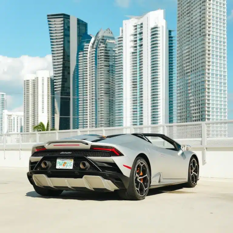 Rear 3/4 view of a silver Lamborghini Huracán EVO Spyder, highlighting its sleek profile and distinct taillights against a city backdrop.