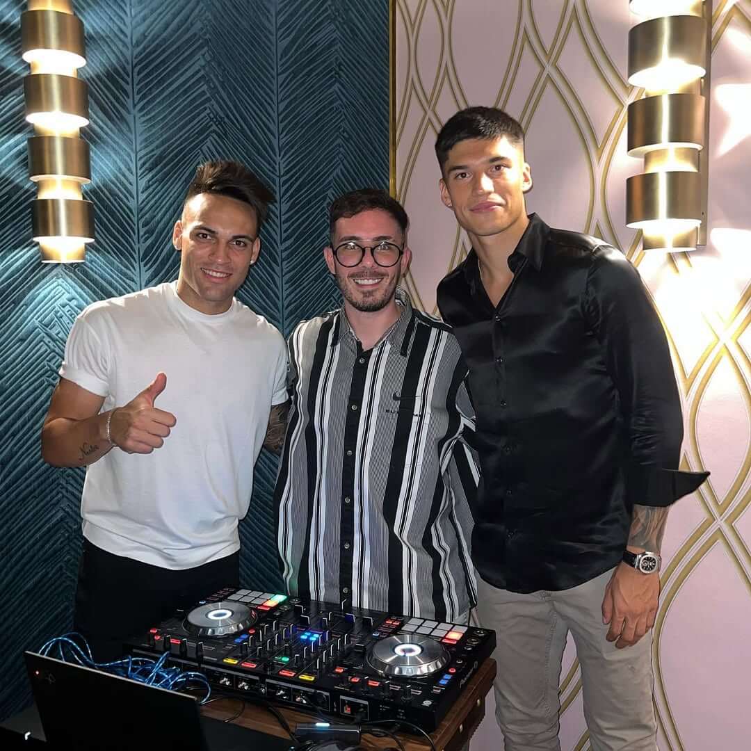 Fer Palacio junto a dos amigos en una cabina de DJ con luces de fiesta en el fondo.