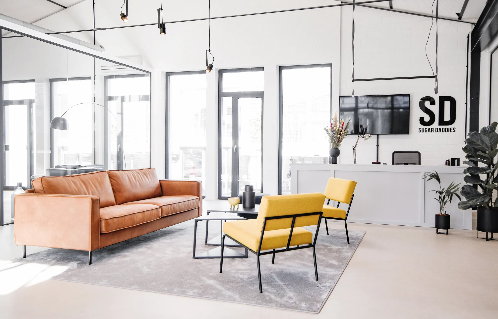 Reception lounge with tan leather sofa, yellow armchairs and SD Sugar Daddies logo wall.