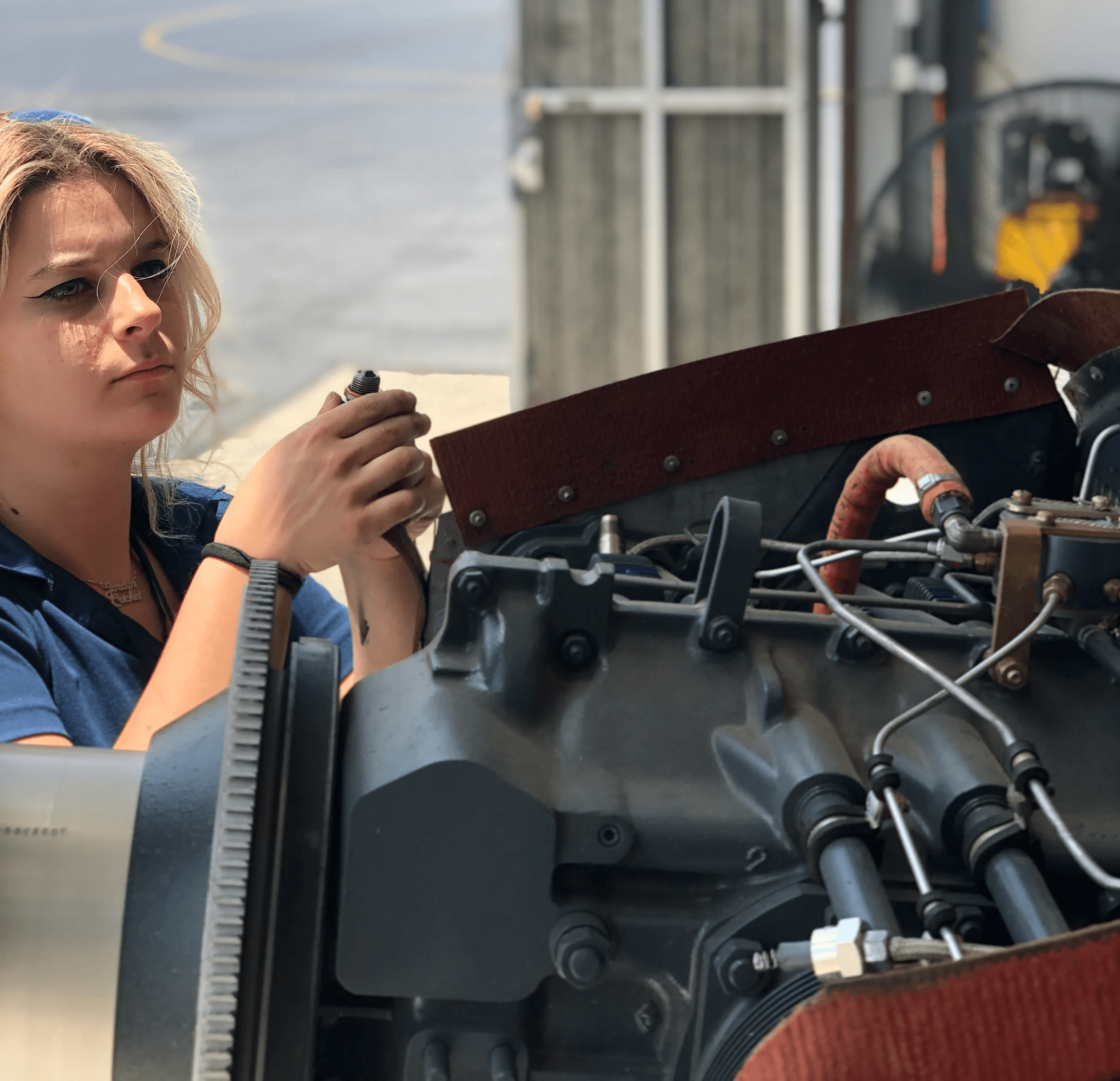 A mechanic performs maintenance on a light aircraft engine inside an open hangar
