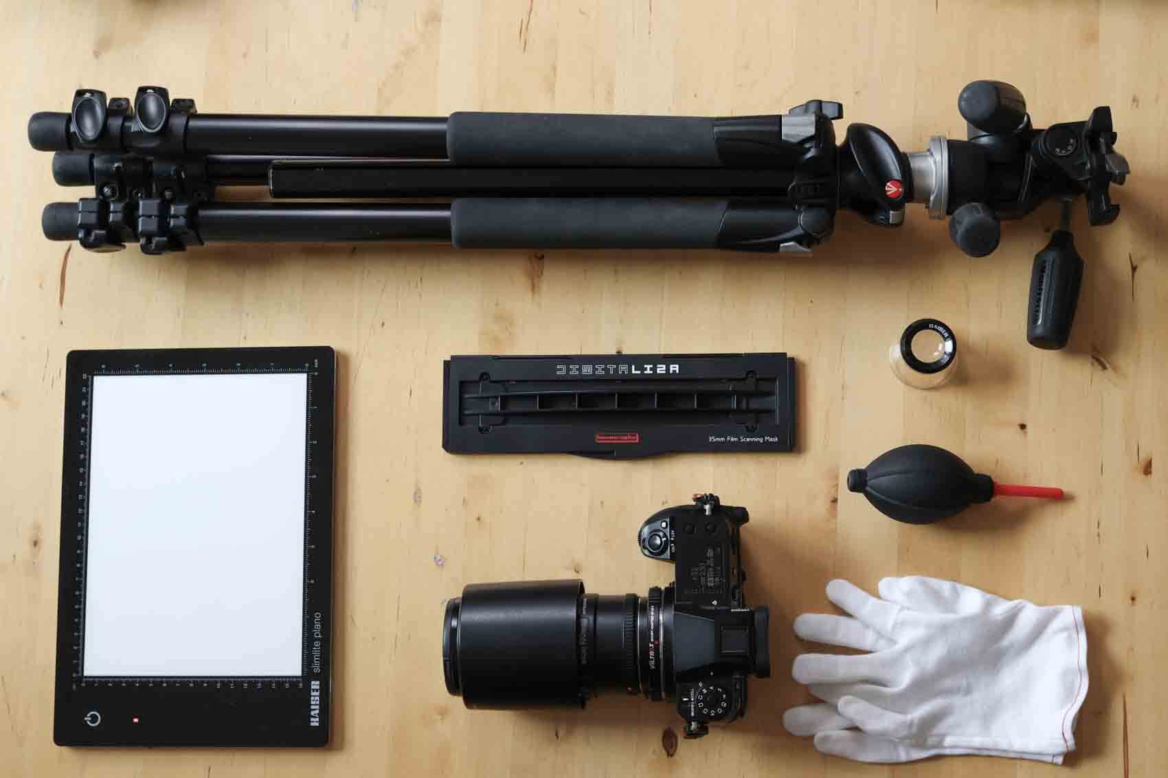 Photography gear layed out on a table, displaying a lightbox, camera, tripod, gloves, airblower and a film holder