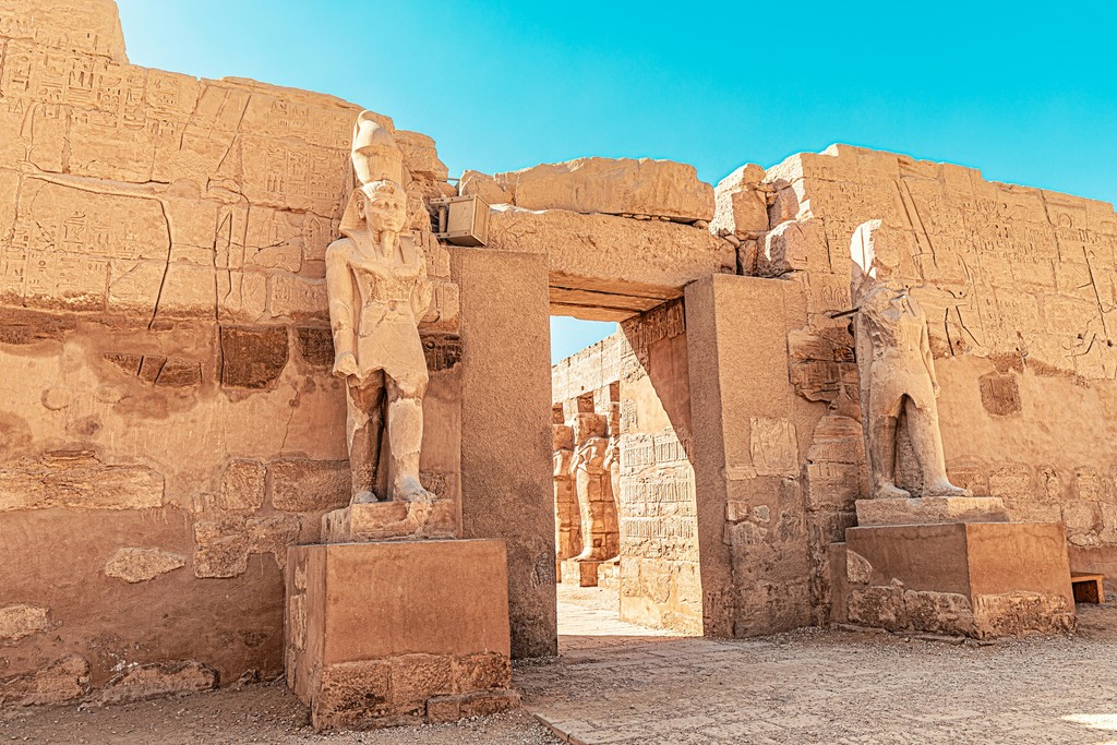 Ancient statues guard the entrance to the Karnak Temple in Luxor, Egypt, showcasing intricate hieroglyphics and the grandeur of historical Egyptian architecture under a clear blue sky.