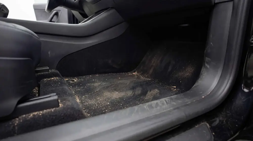 Avant nettoyage des moquettes intérieures d’une Tesla Model Y avec poussières et résidus