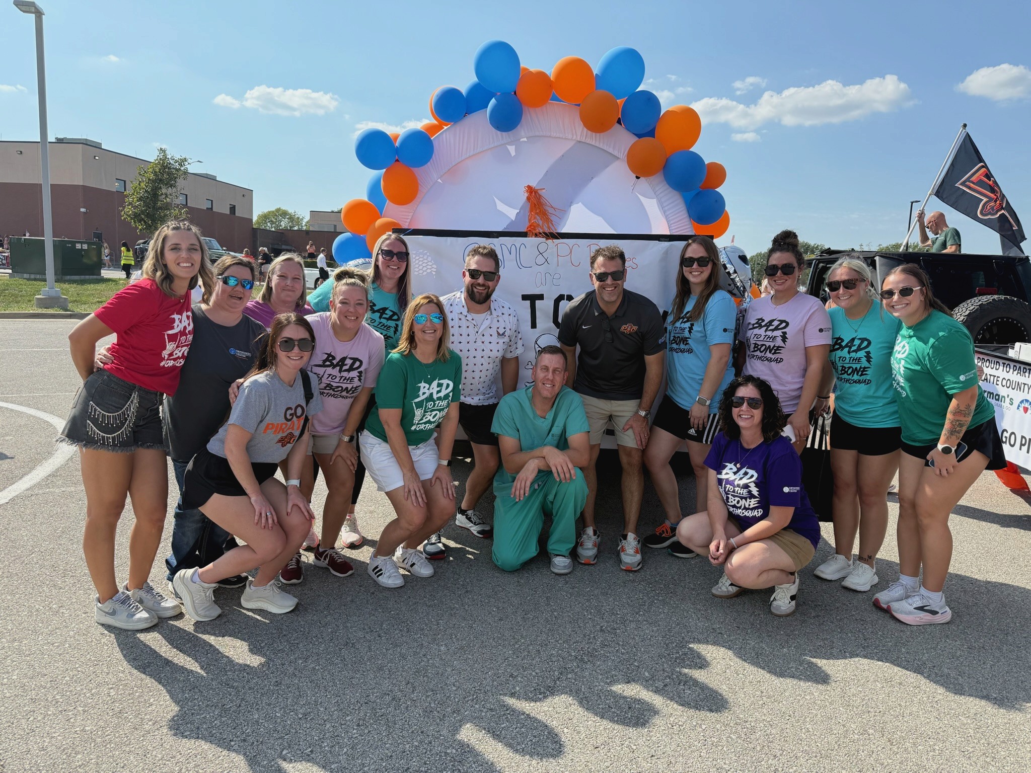 OSMC team and providers at a Northwest Missouri community parade wearing Bad to the Bone OrthoSquad shirts in front of their balloon-decorated float