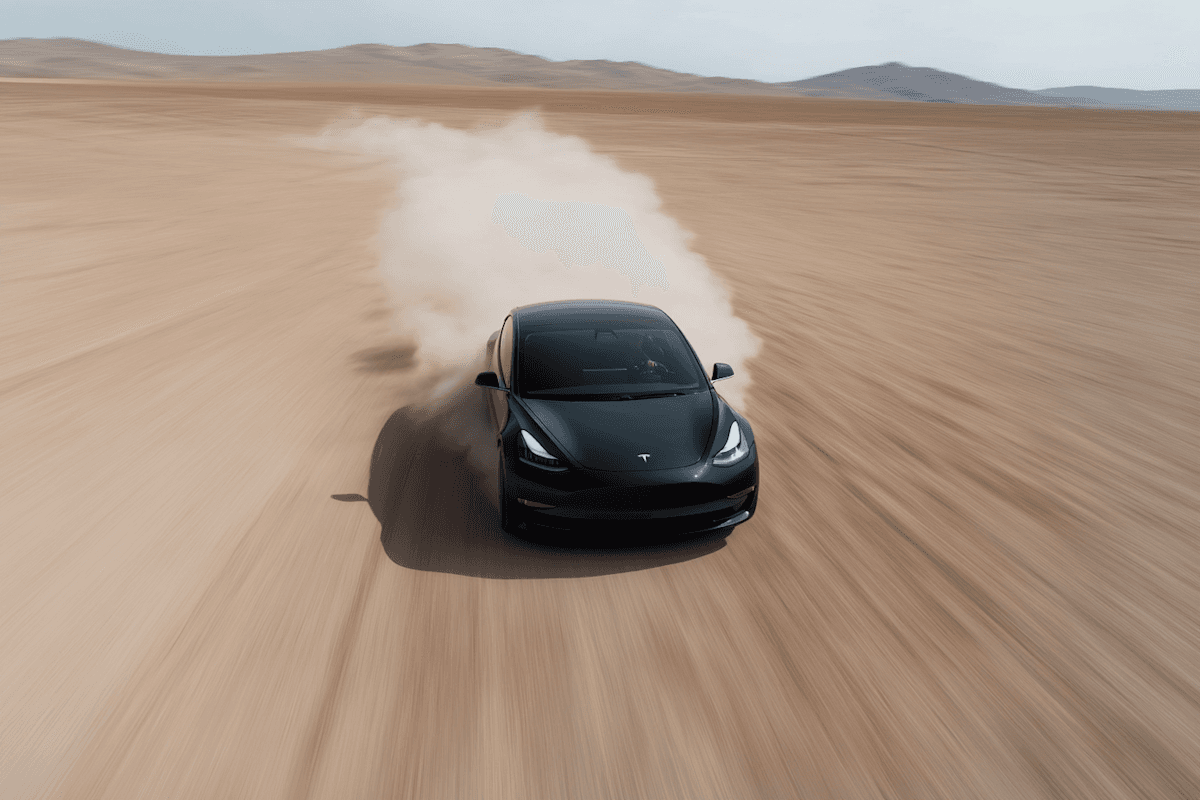 Black Tesla car speeding through a desert, leaving a dust trail, showcasing speed and adventure in a vast, open landscape.