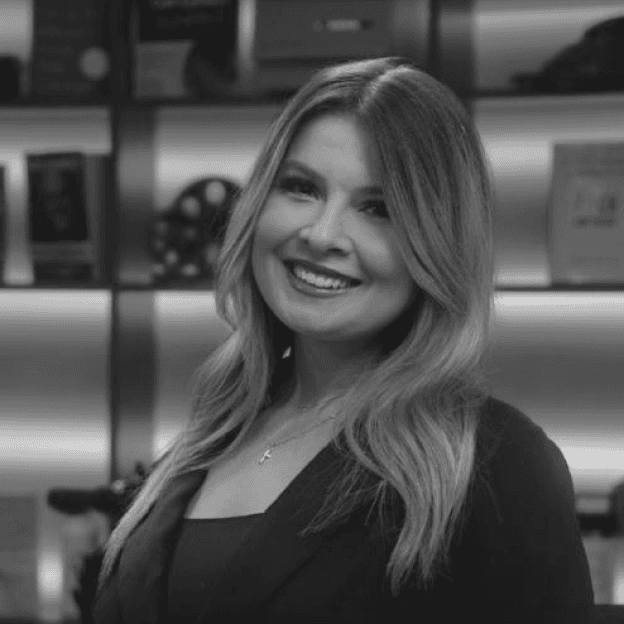 A woman wearing a suit and tie, facing forward, smiling. Formal business attire. Confident look.