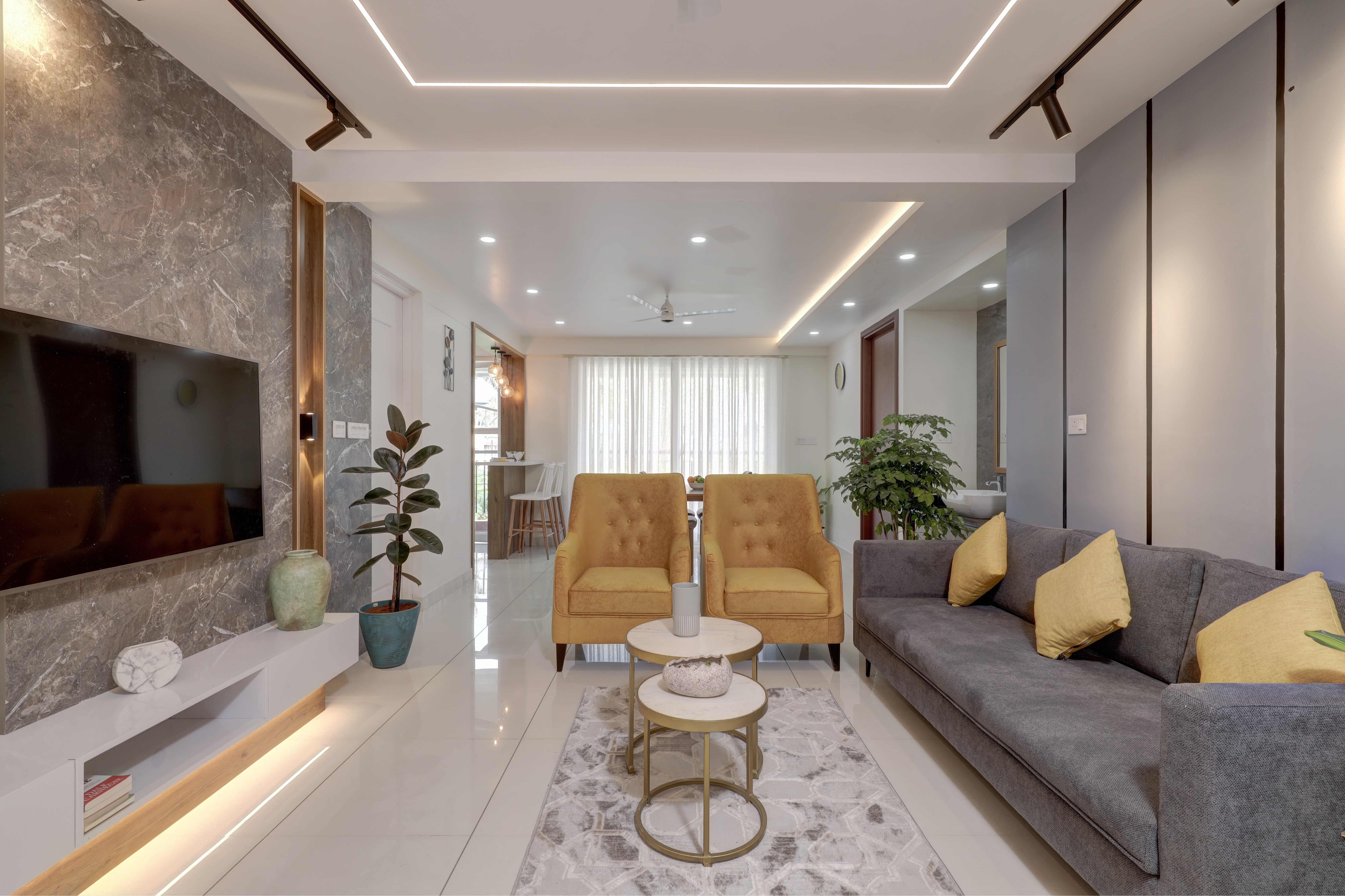 Person in yellow jacket and orange pants sitting on a blue chair, yellow background