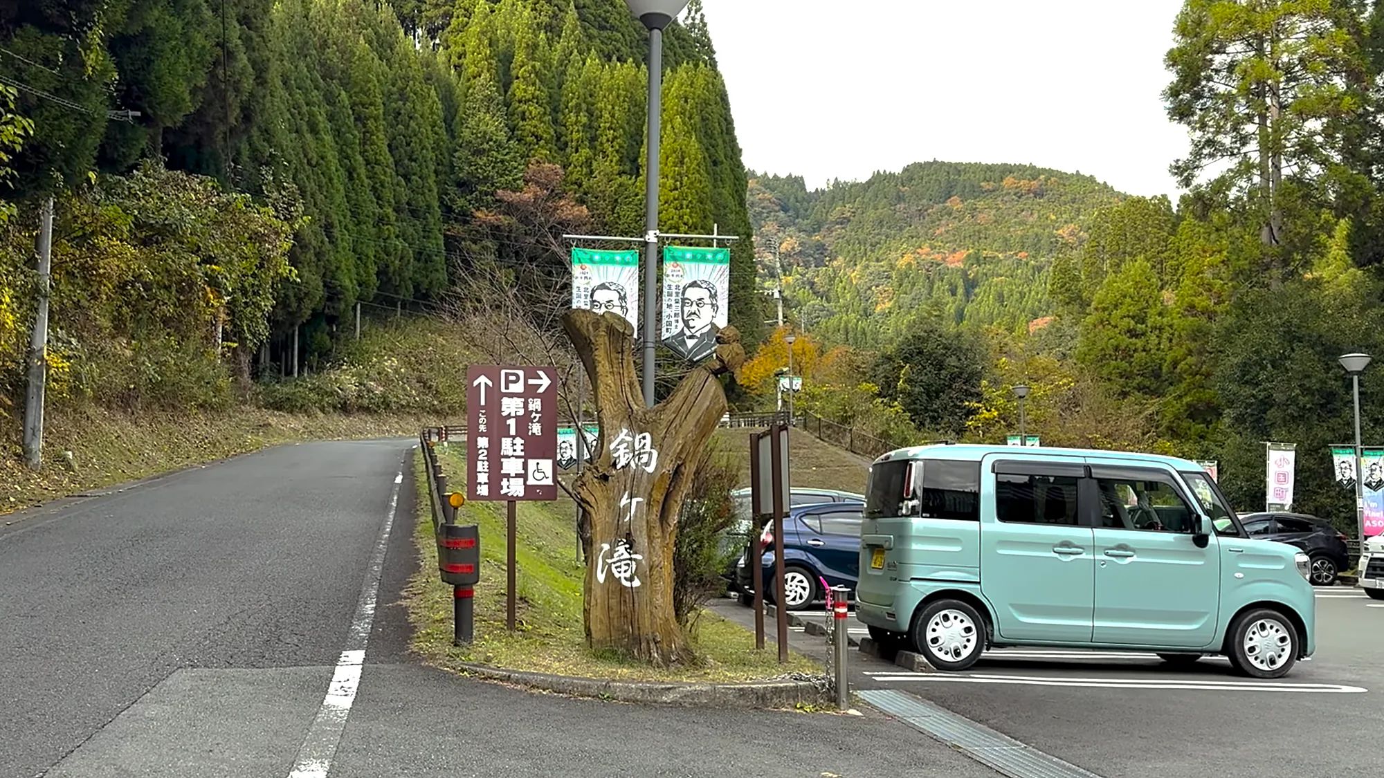 The roadside sign for Nabegataki falls near Kurokawa Onsen, banner flags beside the car park