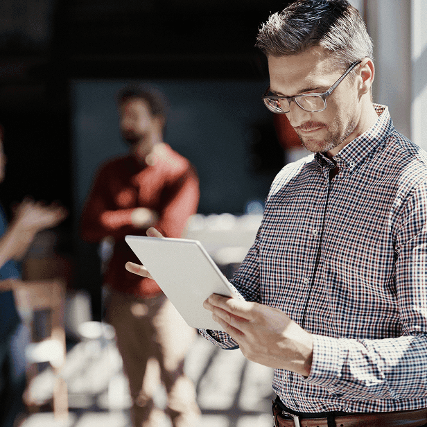 Homem de óculos analisando informações em um tablet em ambiente de trabalho.