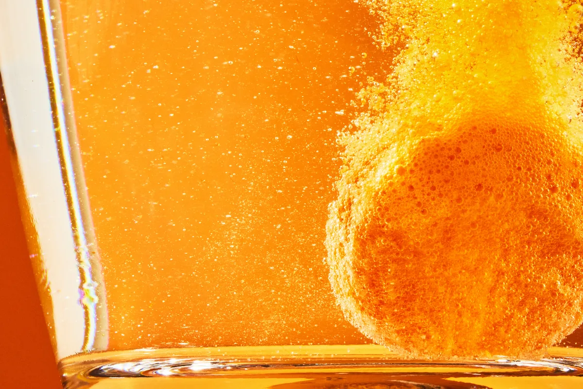 An orange Vita Soda tablet fizzing as it dissolves in a glass of water, close up