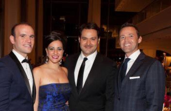 A woman in a blue gown stand with three men in tuxedos at a Gala event.
