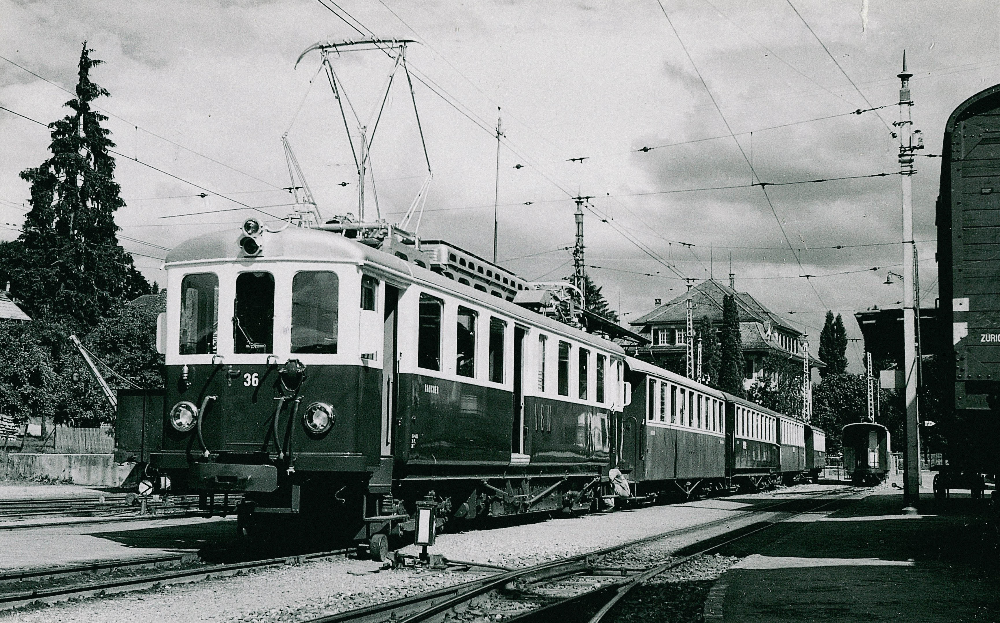 Schwarz Weisses historisches Bild von einem Triebwagen an einem Bahnhof. 
