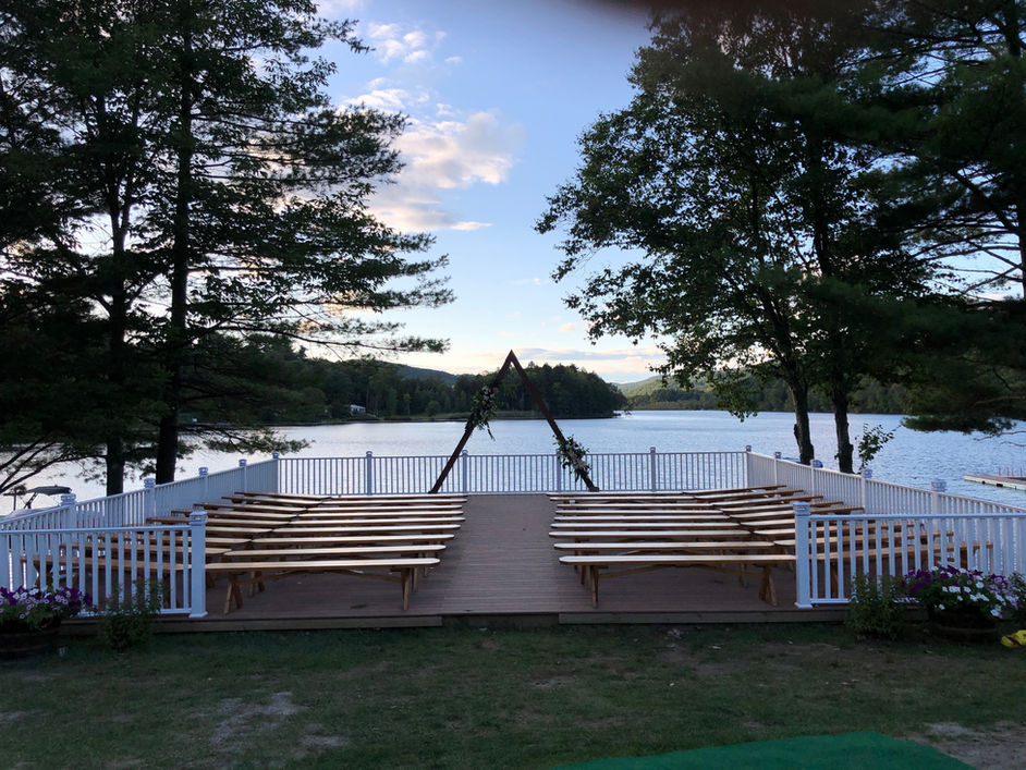 Lakeside ceremony deck with wooden benches and arch at sunset at Camp Lenox