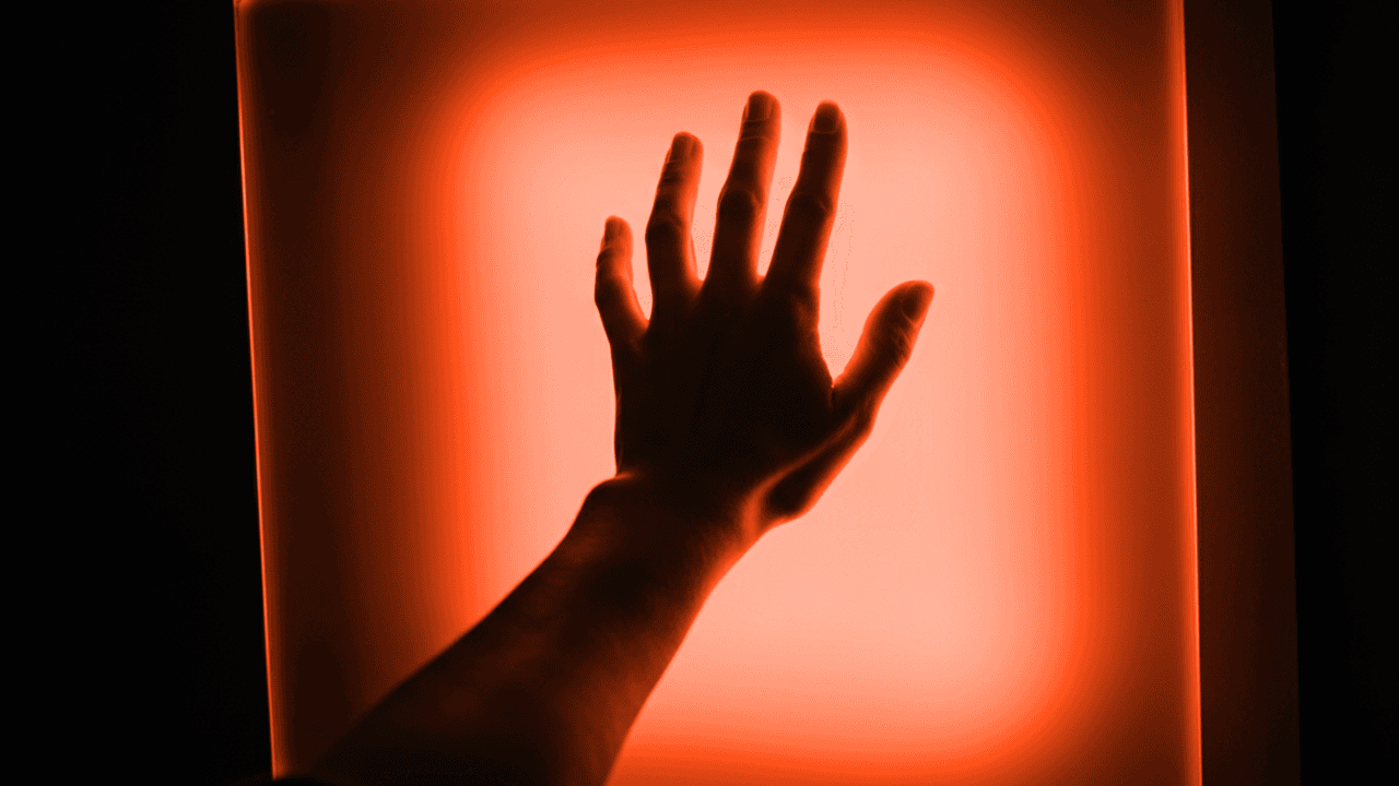 Person's hand touching a bright orange, glowing light source. Warmth and illumination.