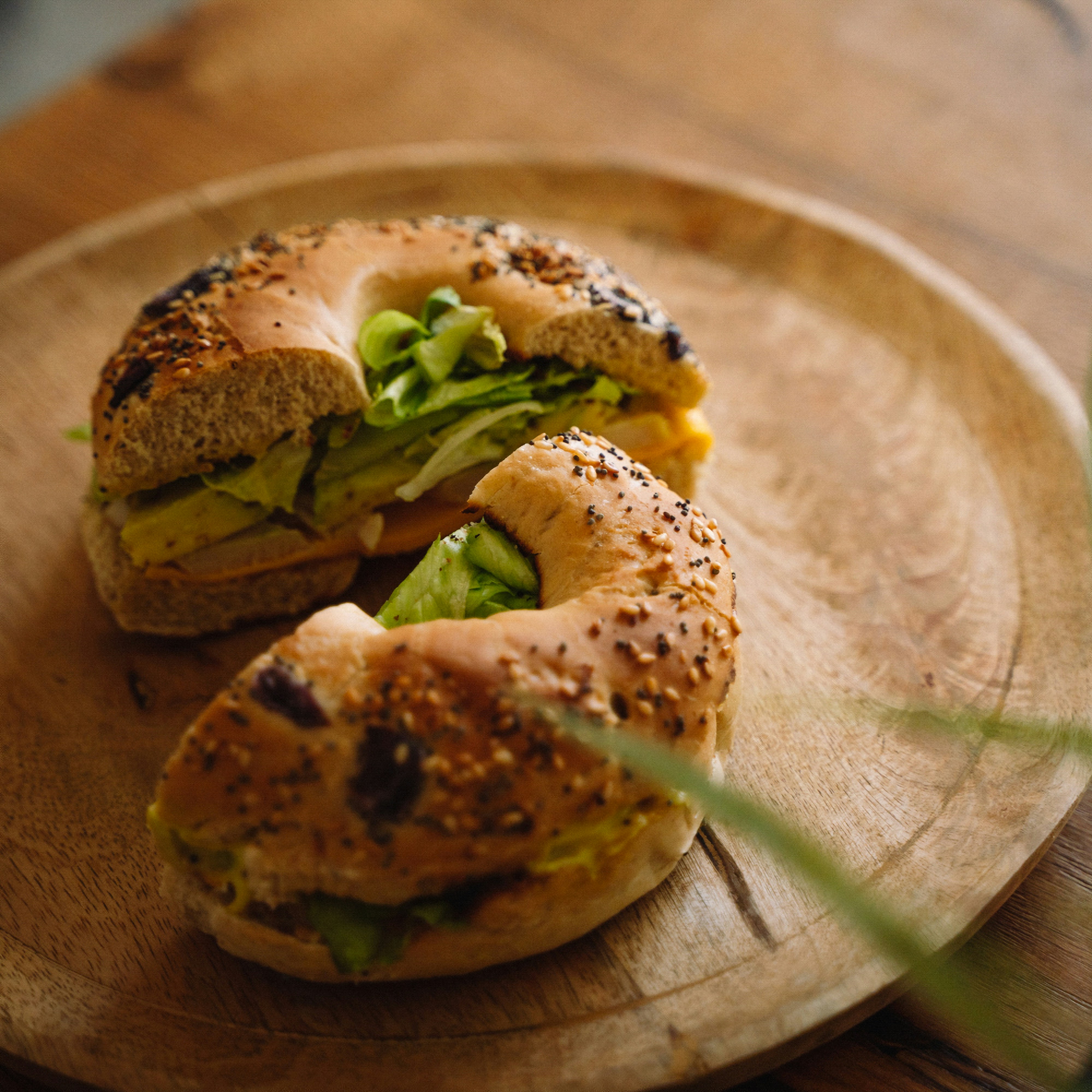 A toasted bagel topped with avocado slices and herbs, served on a wooden plate with a rustic background.