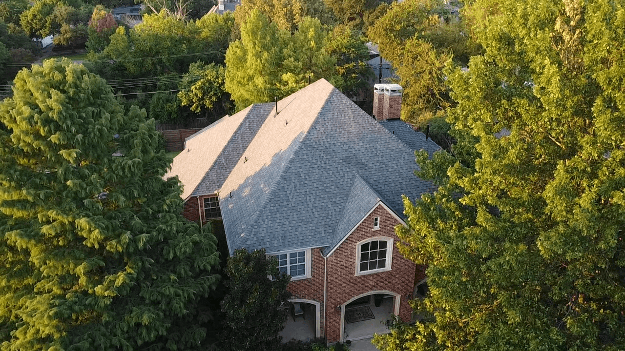 residential roofing services in Arlington showcasing a completed shingle roof on a large brick home surrounded by trees.
