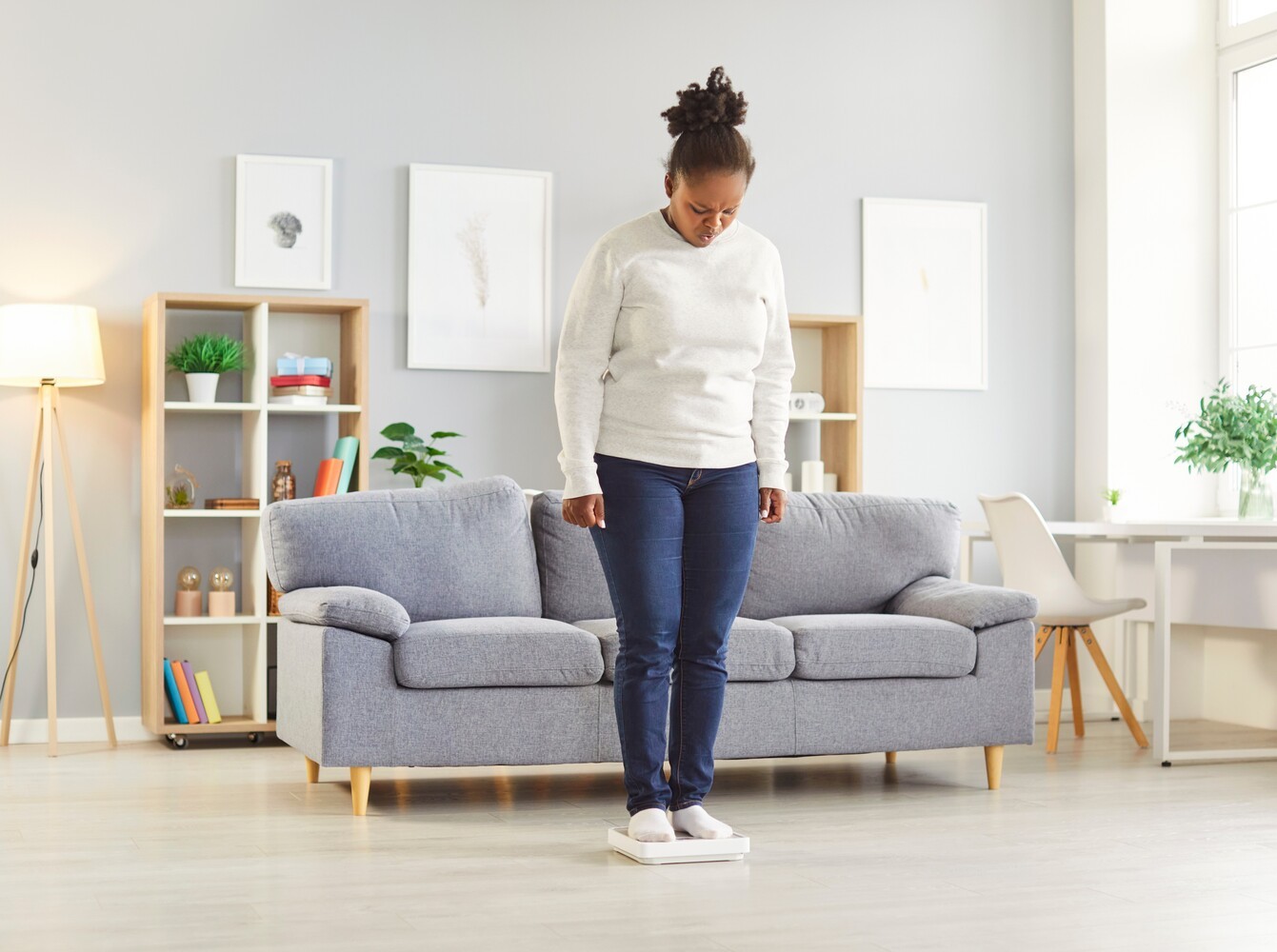 woman measuring her progress on a scale in her living room after doing pilates and weight loss