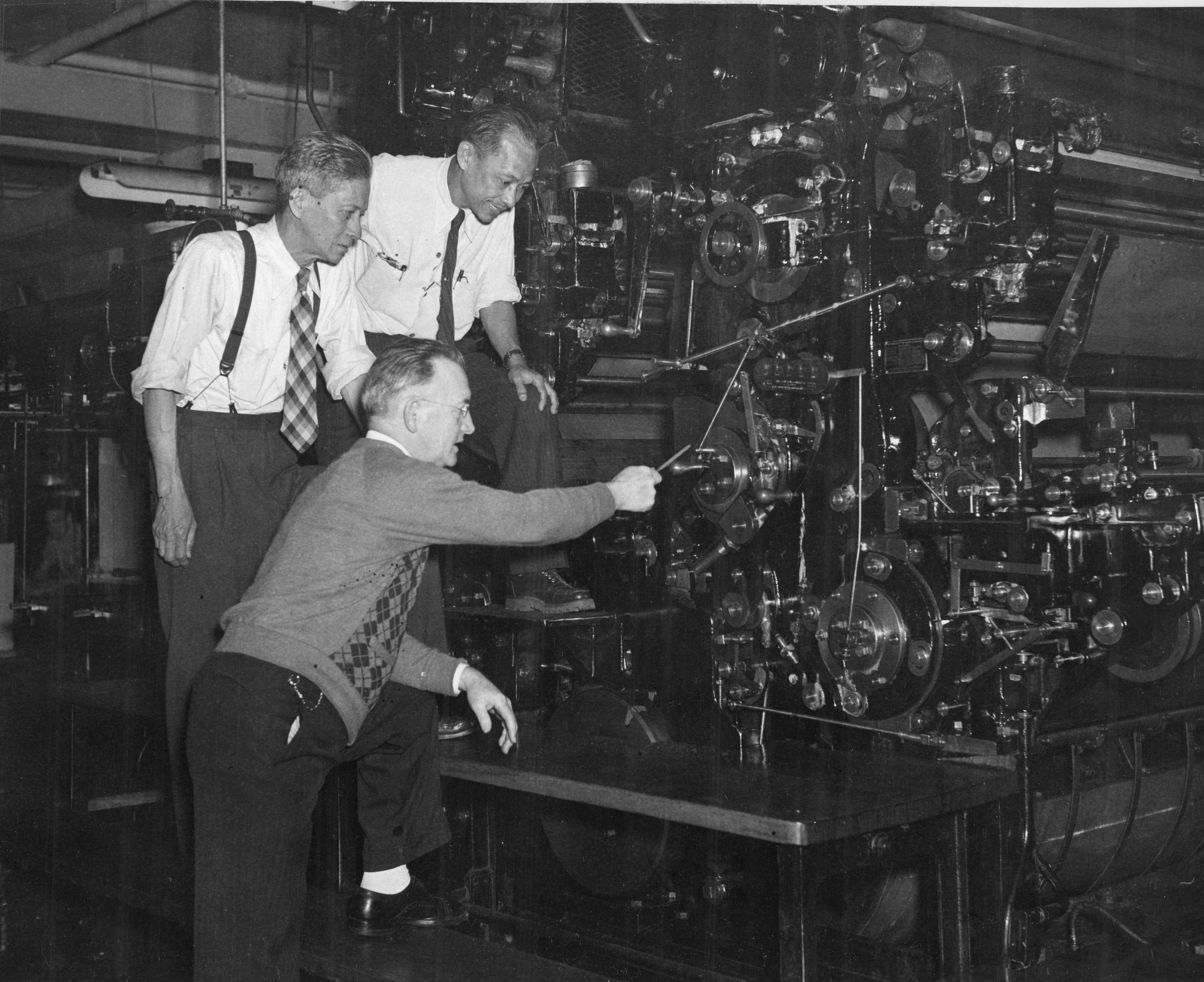 Three men fixing a machine in a factory
