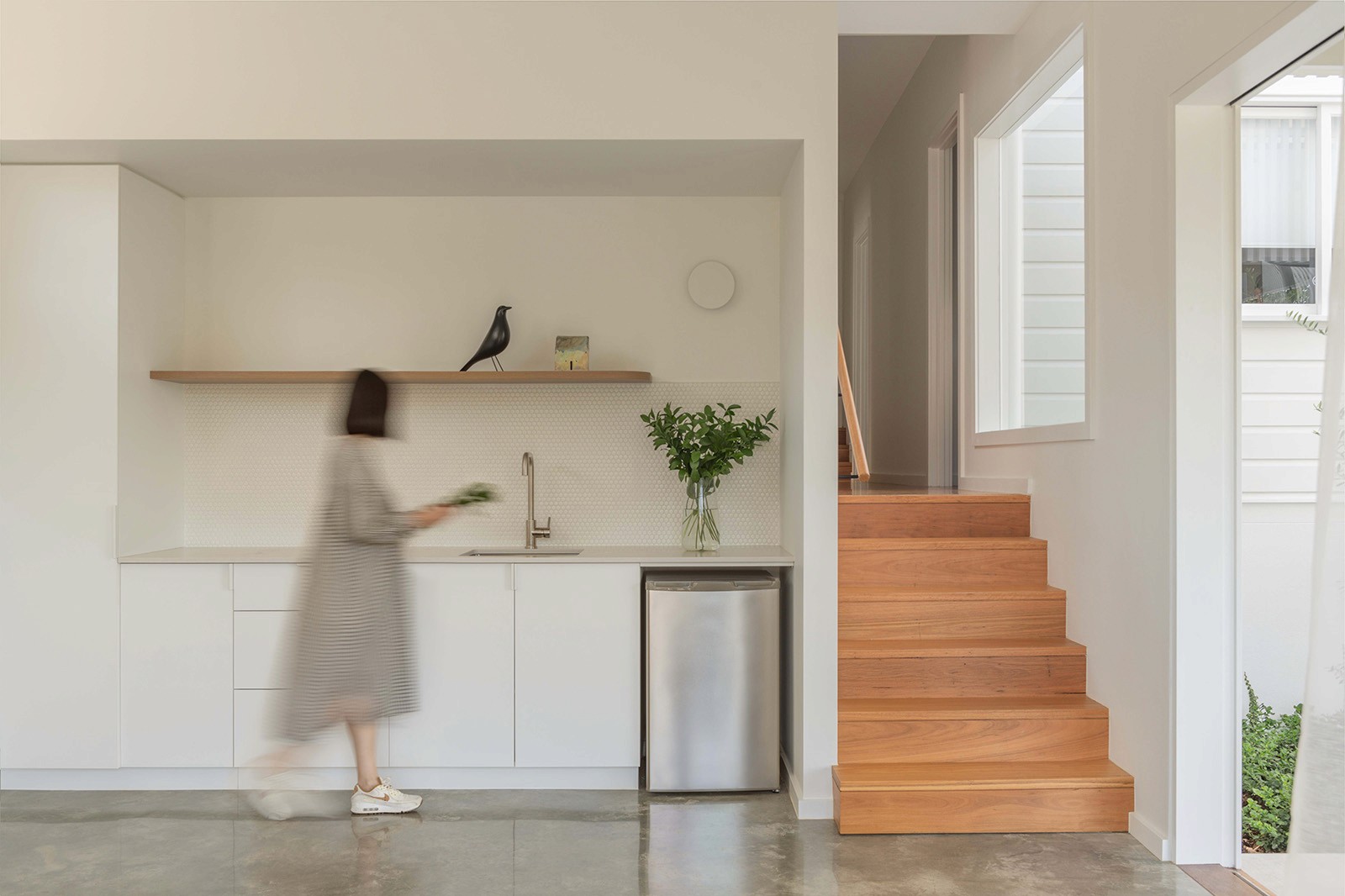 Light-filled utility space with integrated sink, open shelving, stainless fridge, and timber stair connecting to upper level.