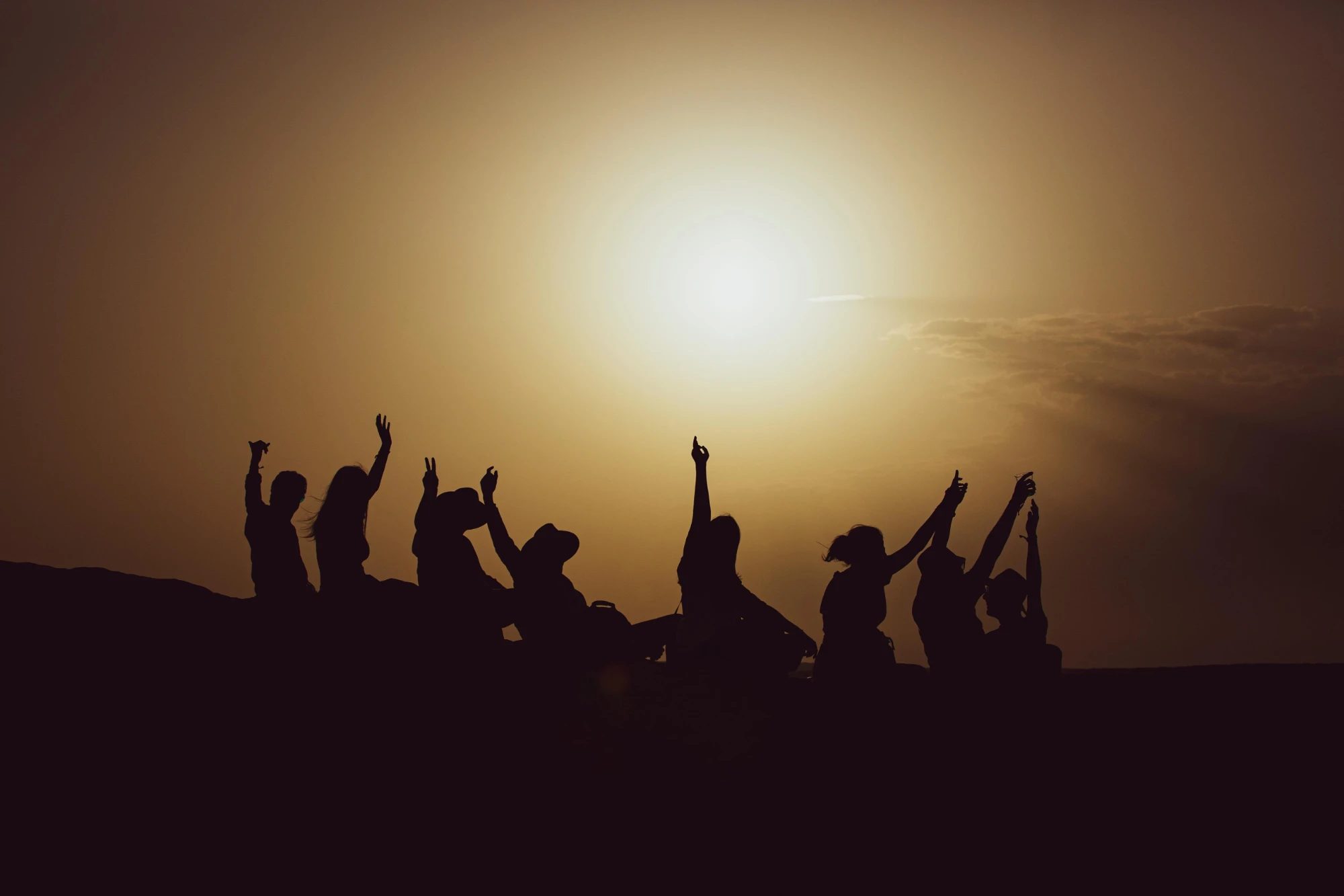 Friends with raised arms on a dune at sunset