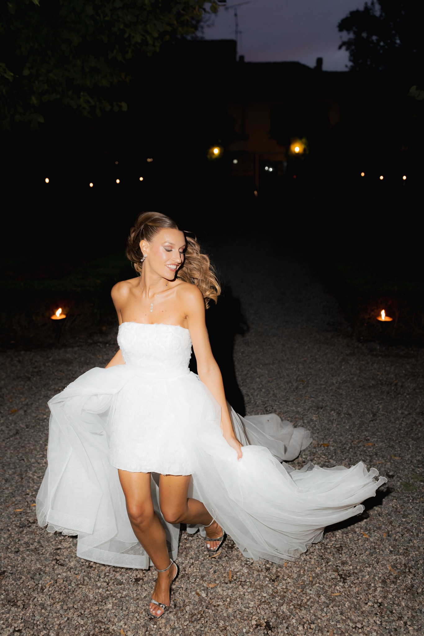 Sposa in abito bianco a spalla nuda balla nella corte di Villa Ferrari, velo che svolazza, luci calde al tramonto