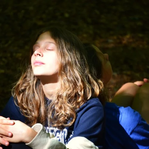 Ragazza seduta nel bosco con occhi chiusi durante esperienza di educazione outdoor e consapevolezza