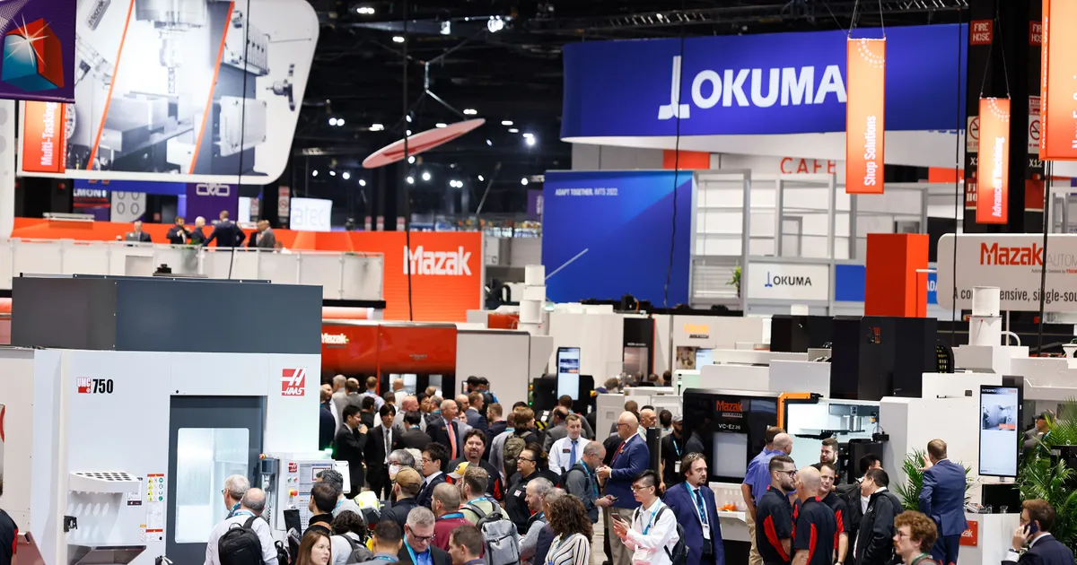 Large industrial trade show booth at IMTS Chicago inside McCormick Place with heavy machinery display and overhead rigging structure