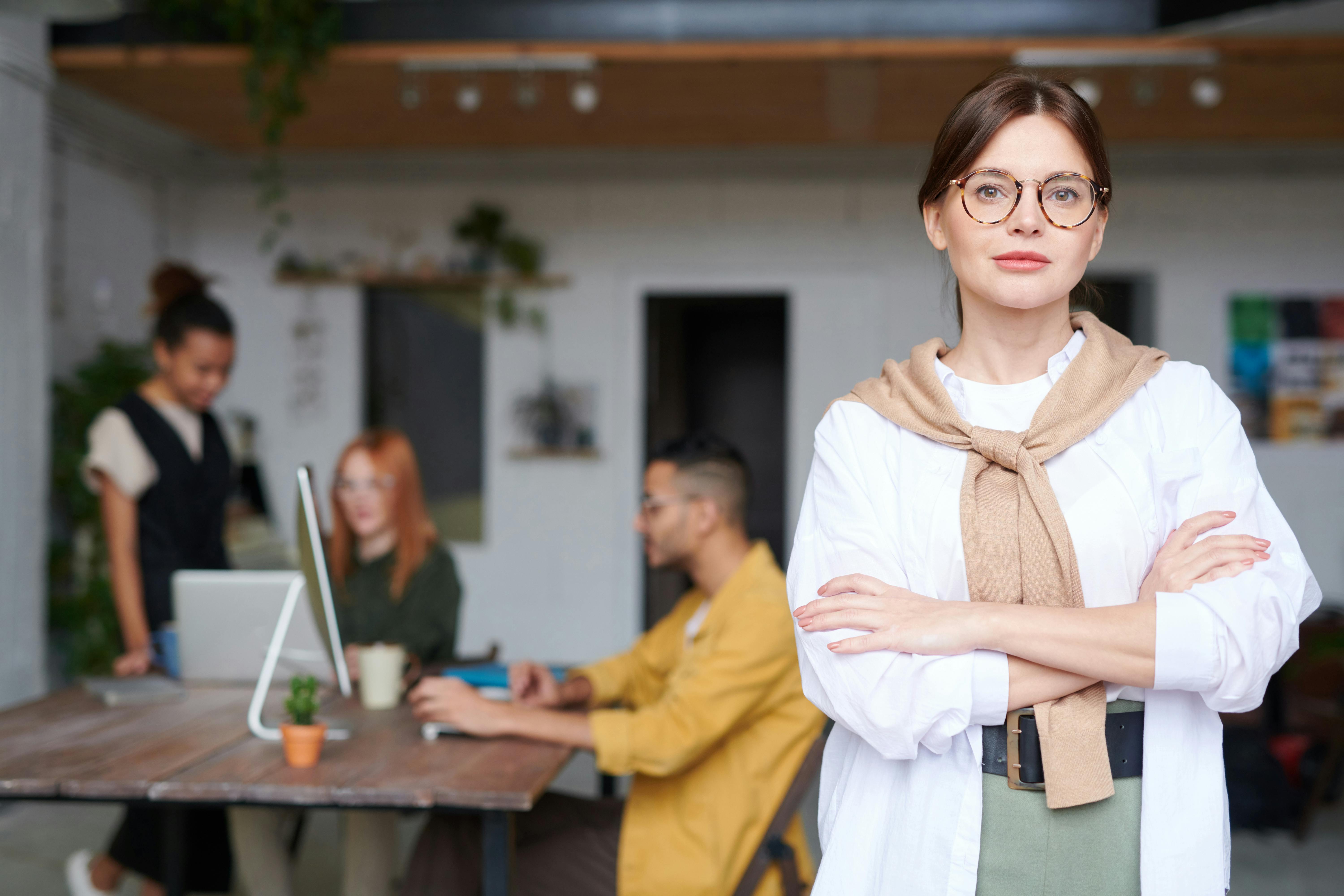 A woman in professional clothing with  group of people working in an office  in the background