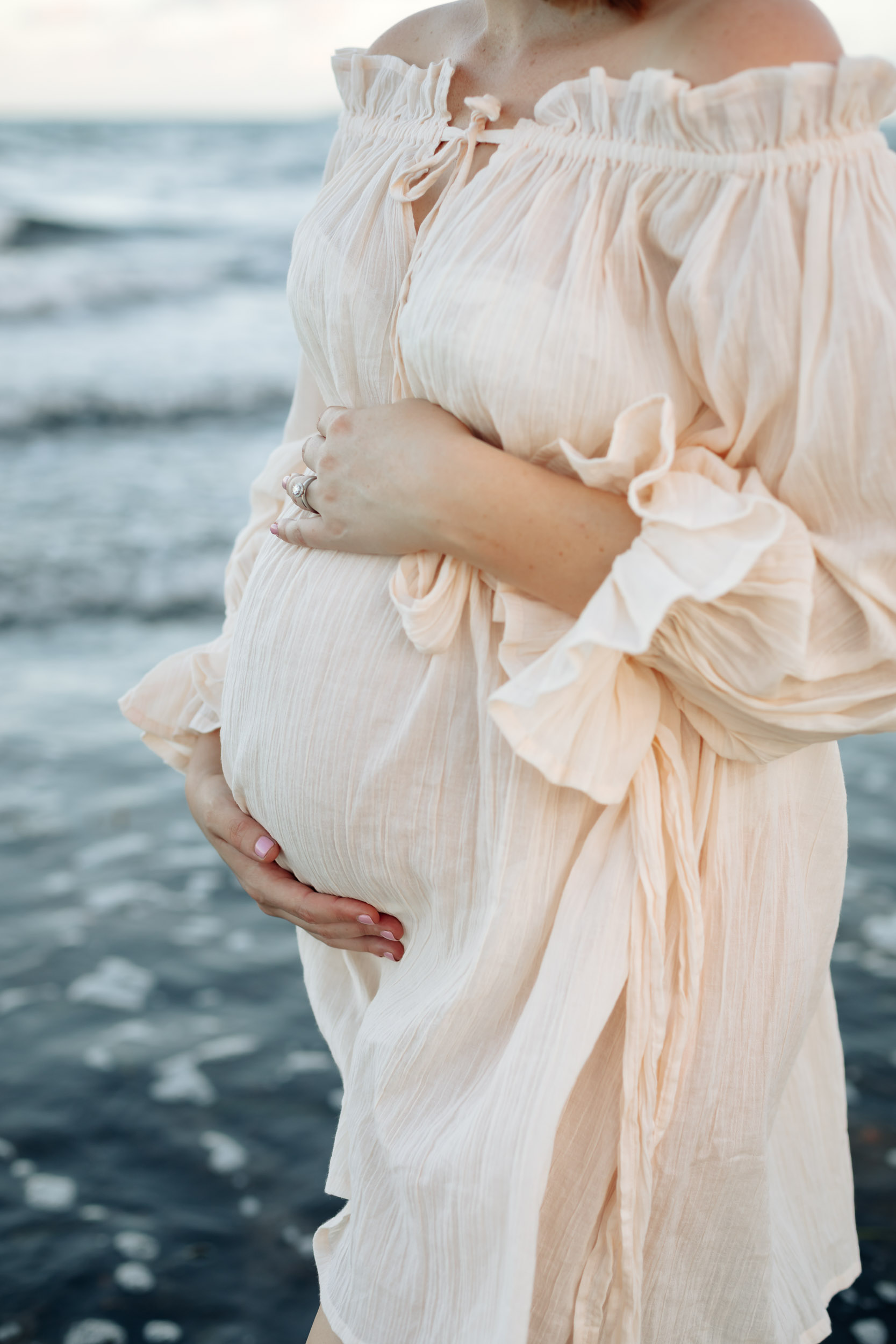 Expecting mother in flowing dress photographed at sunset on a Mackay beach during a solo maternity photography session.
