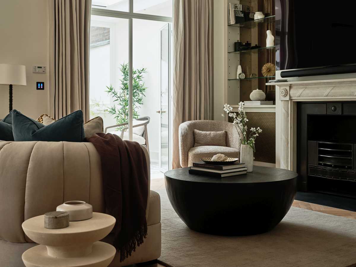 Contemporary Islington lounge area designed by Doll & Co. featuring a channel-tufted sofa, round black coffee table, traditional fireplace, and floor-to-ceiling drapery.