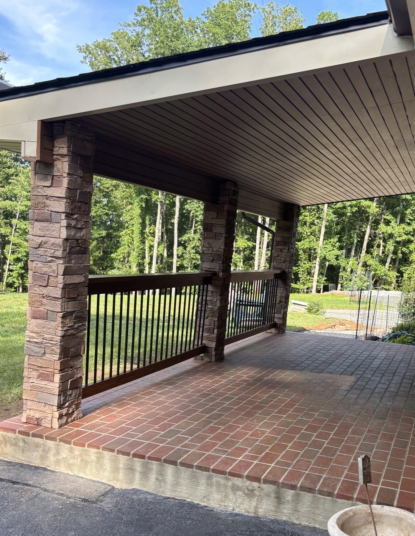 Covered porch with stone columns, brick paver floor and a stained rail