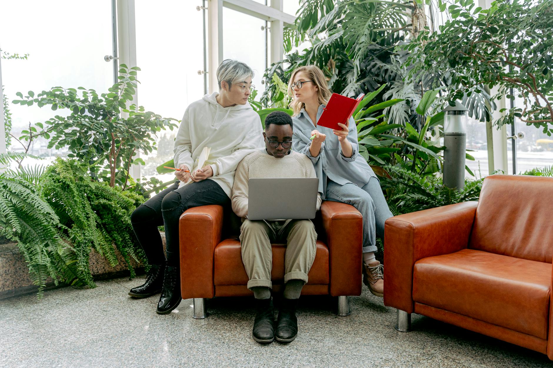A middle school student wearing headphones sits on a living room sofa while studying on a laptop.